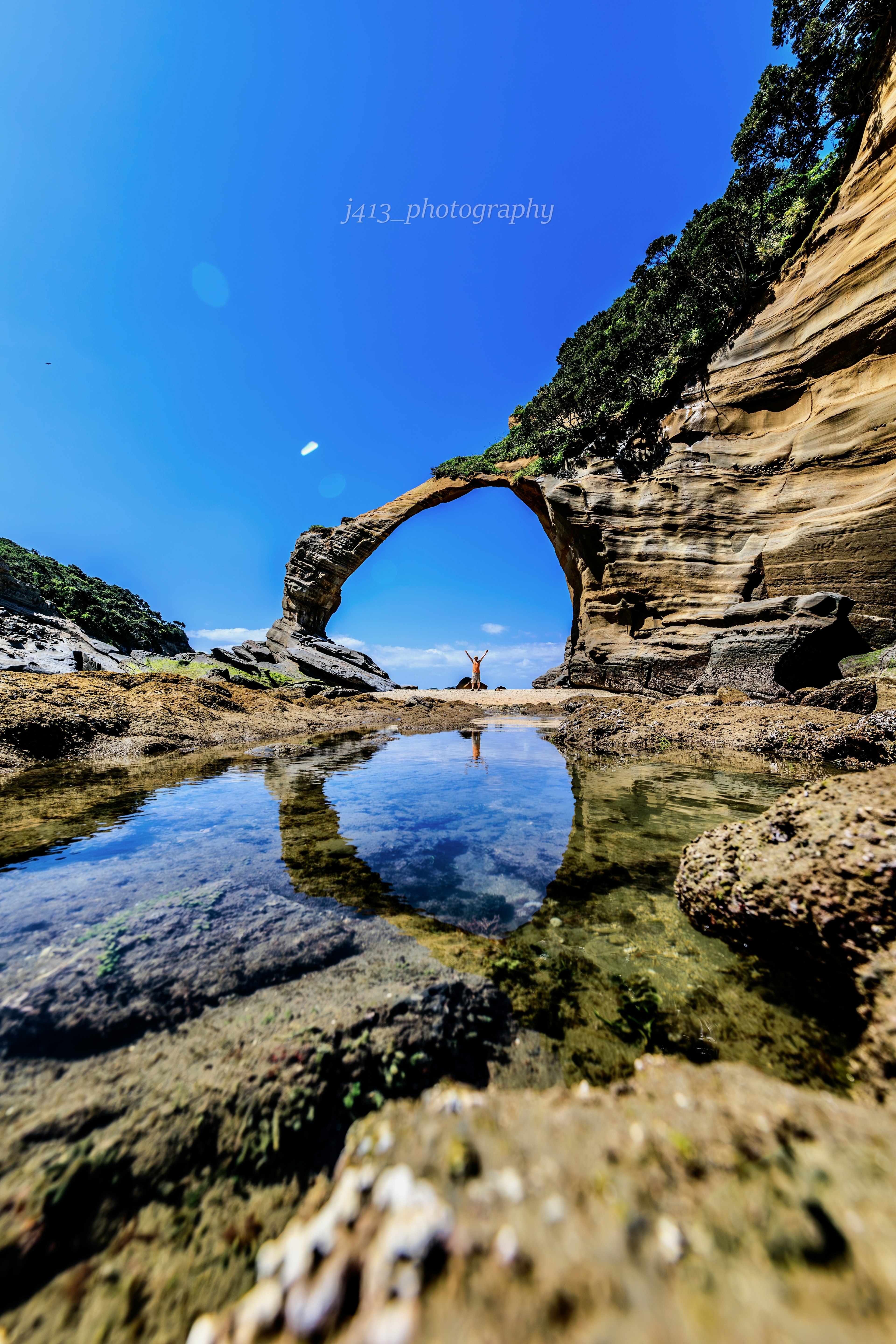 Arc naturel sous un ciel bleu clair avec réflexion dans une flaque d'eau