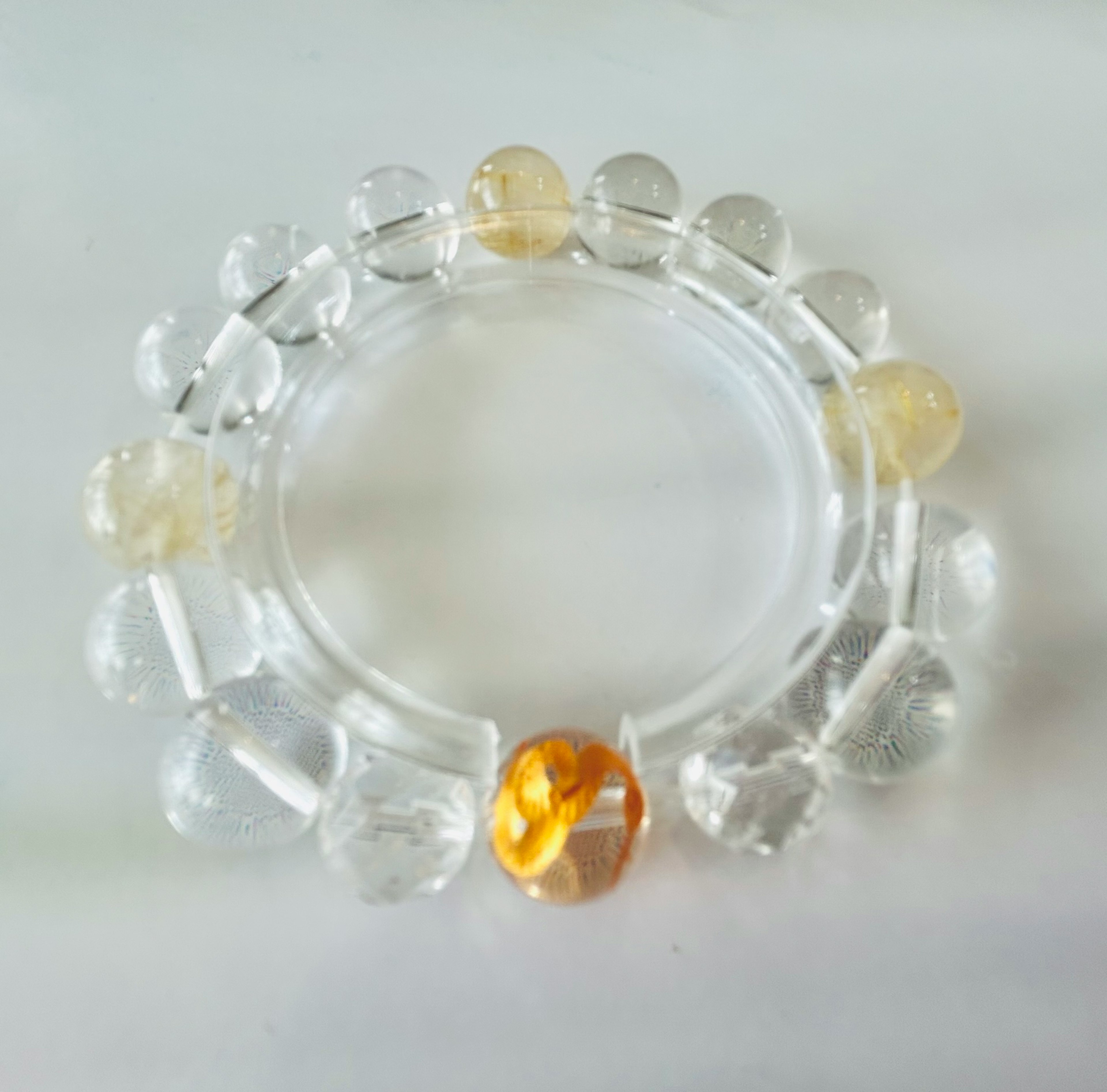 A circular bracelet made of crystal beads featuring clear and one orange bead