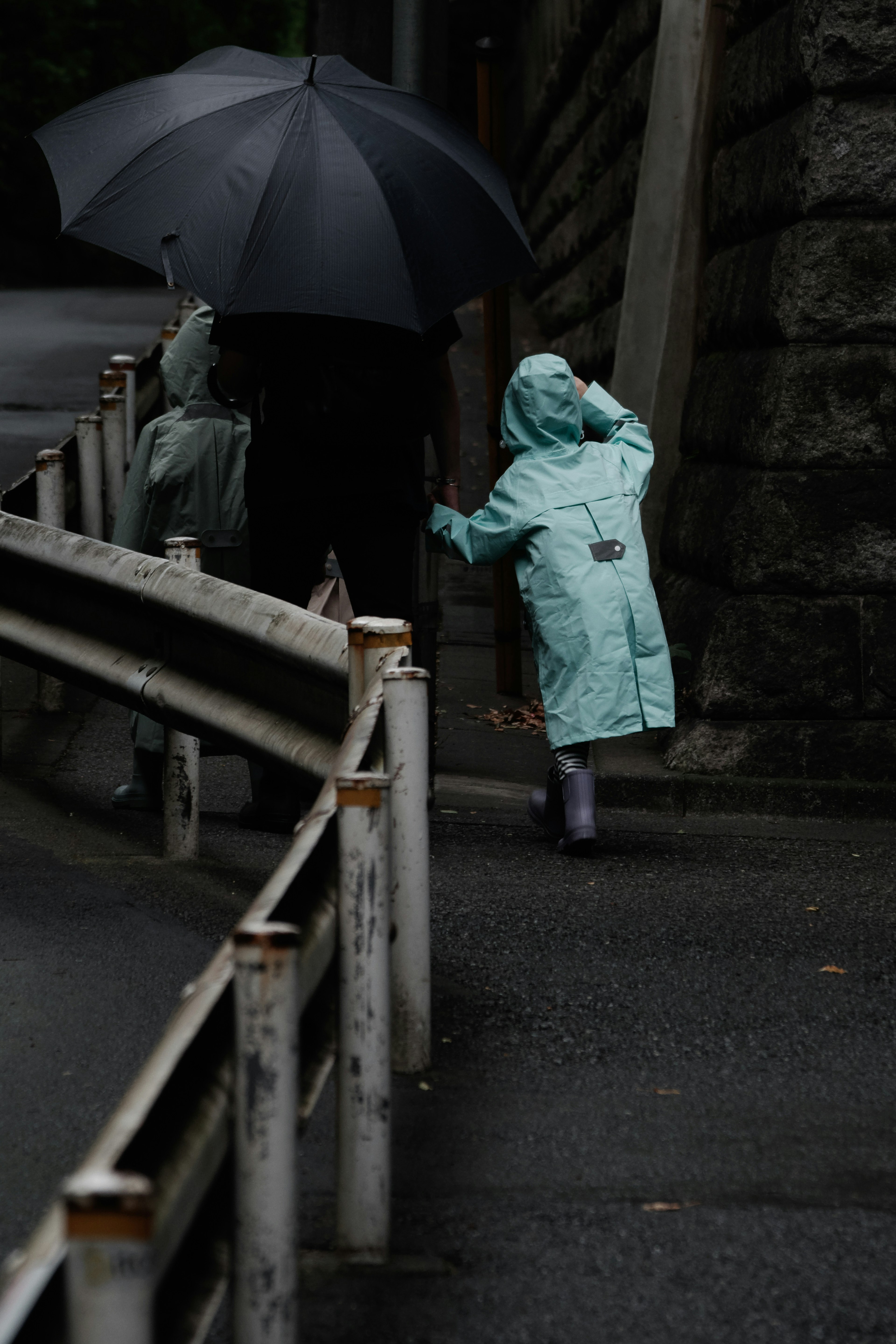 在雨中行走的人們撐著雨傘和穿著藍色雨衣的孩子