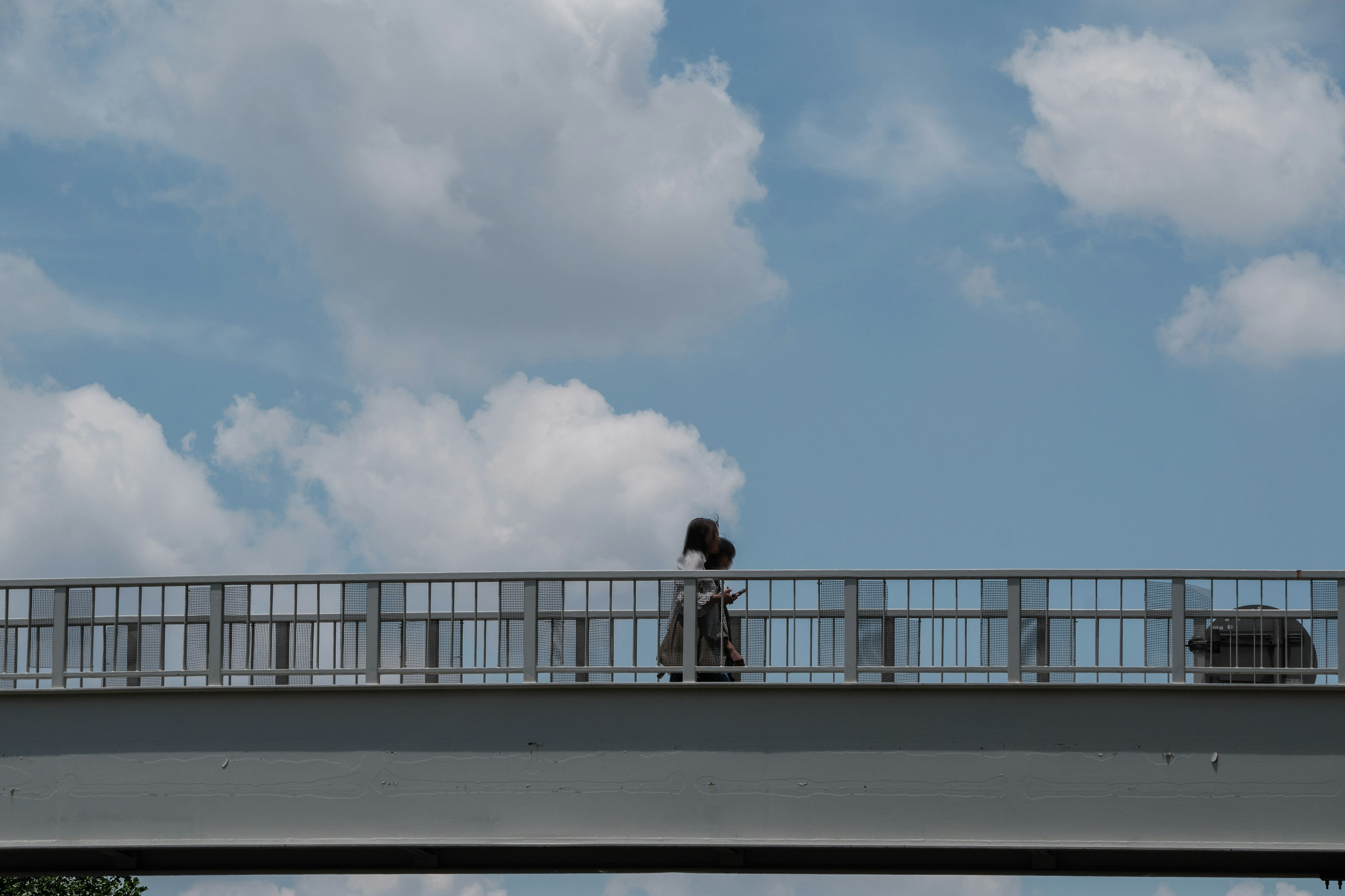 Silueta de una persona caminando sobre un puente bajo un cielo azul