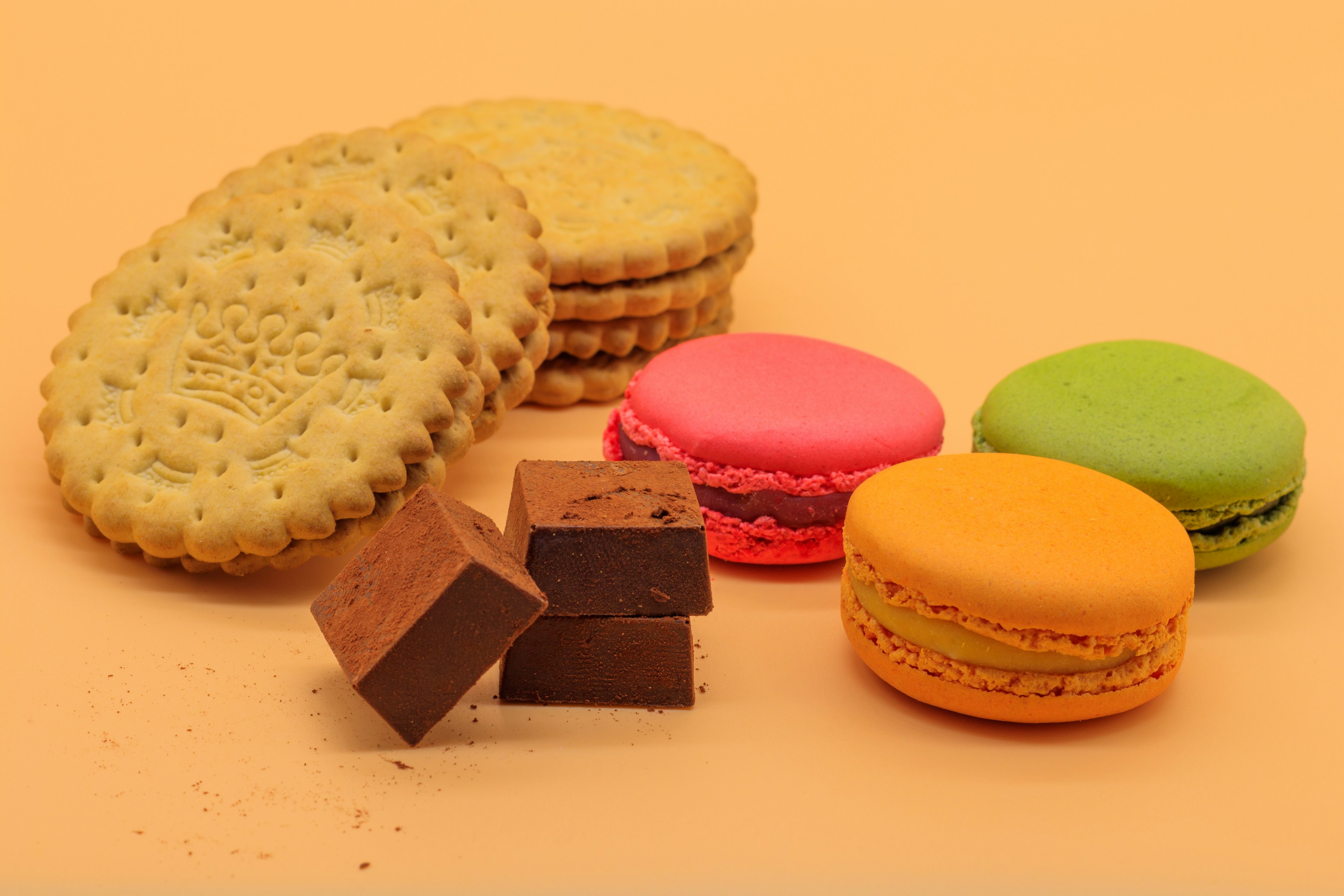 Macarons colorés et cubes de chocolat disposés sur un fond orange