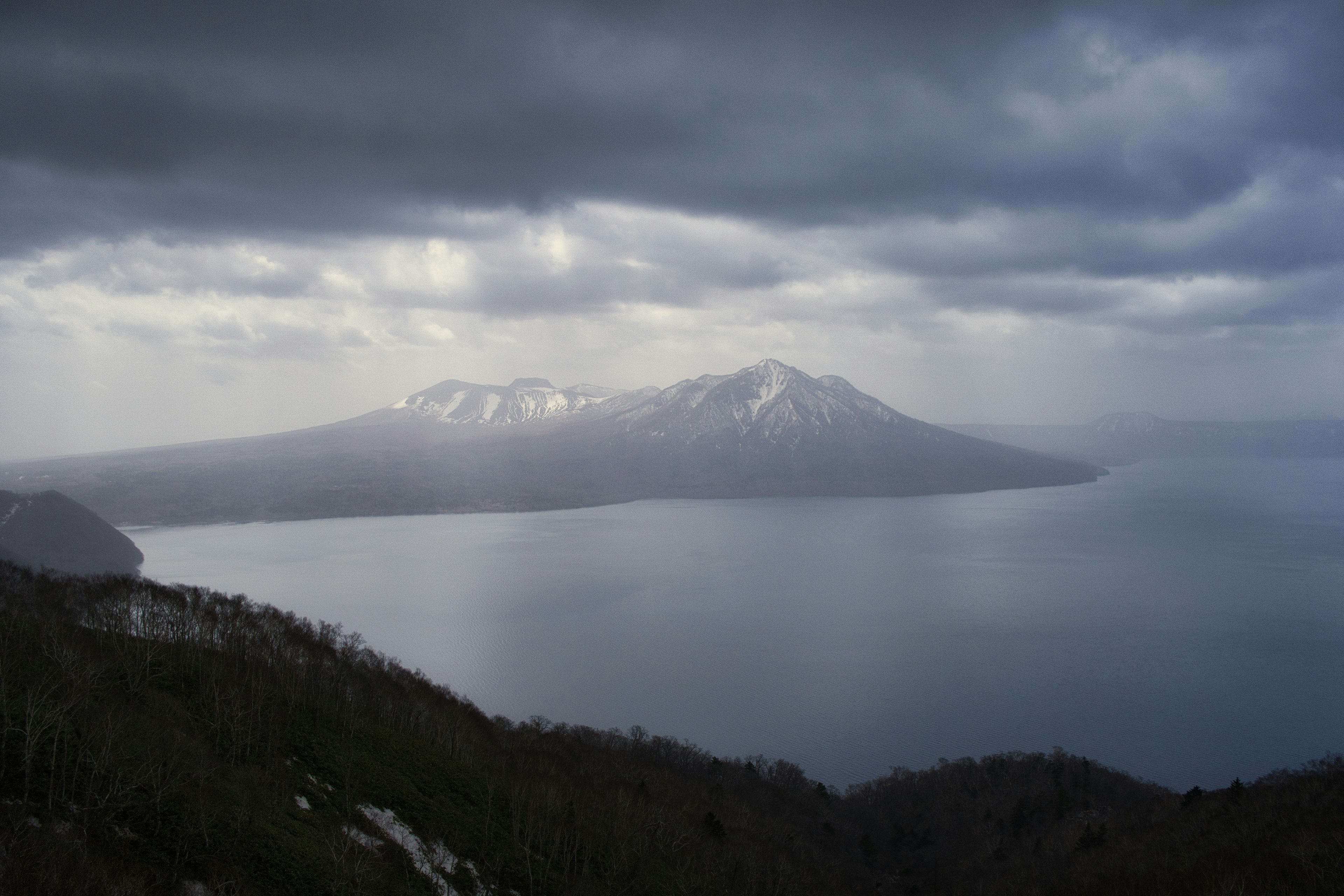 Vista del lago rodeado de montañas nevadas y nubes oscuras