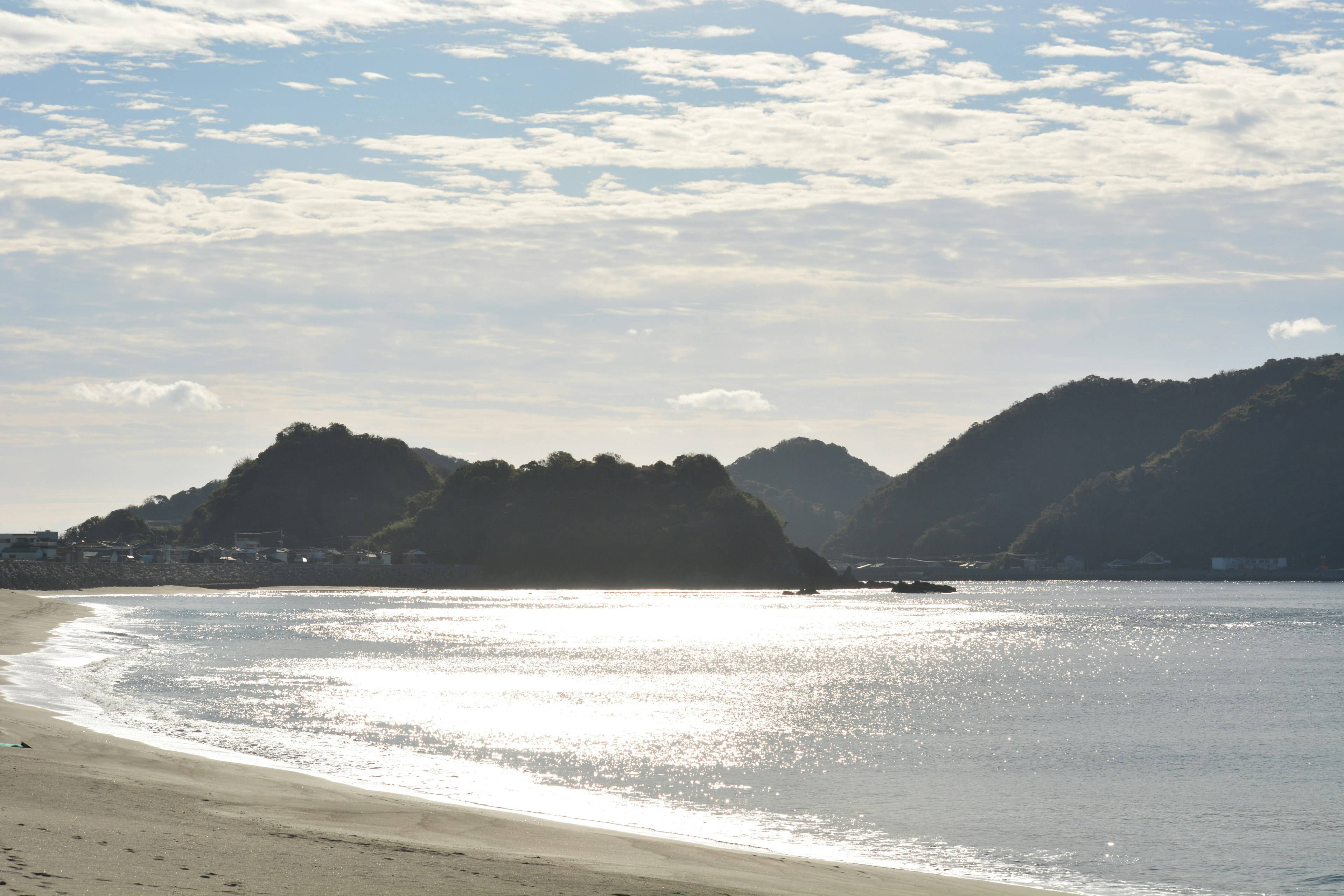 Coastal scene with mountains shimmering water surface clouds in the sky