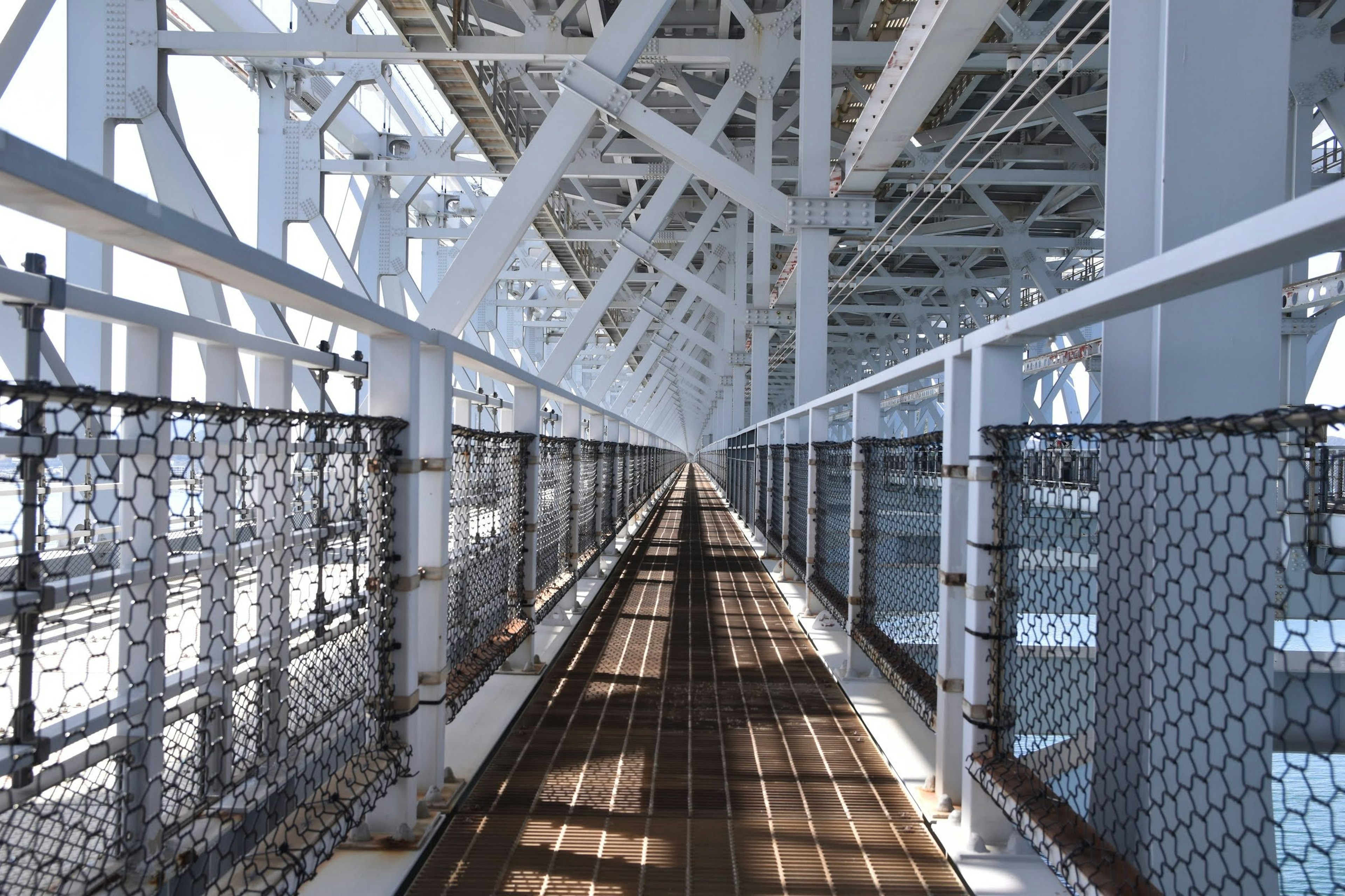 Wooden walkway with chain-link fence under a white steel structure