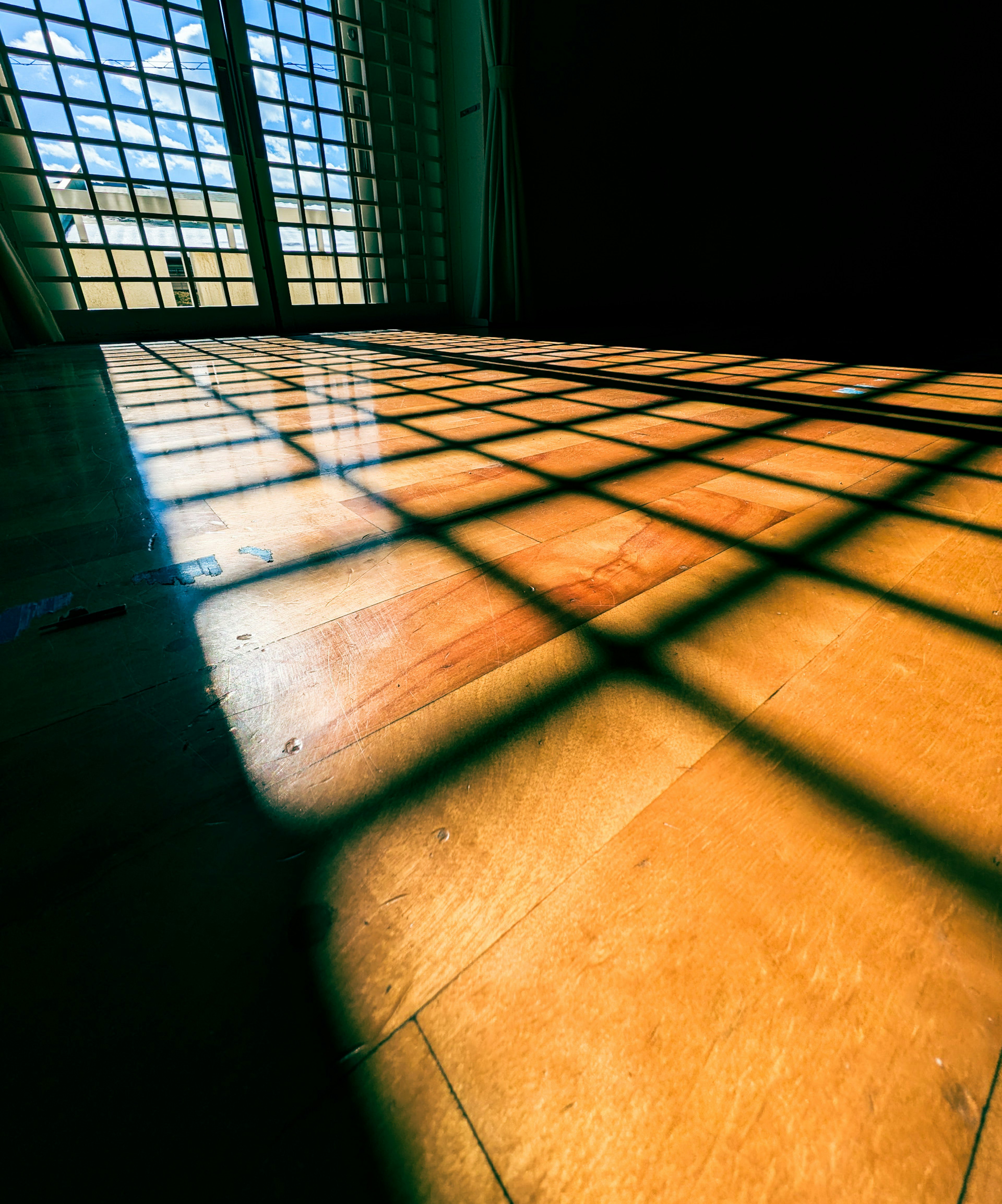 Escena interior con luz solar proyectando sombras en cuadrícula sobre el suelo de madera