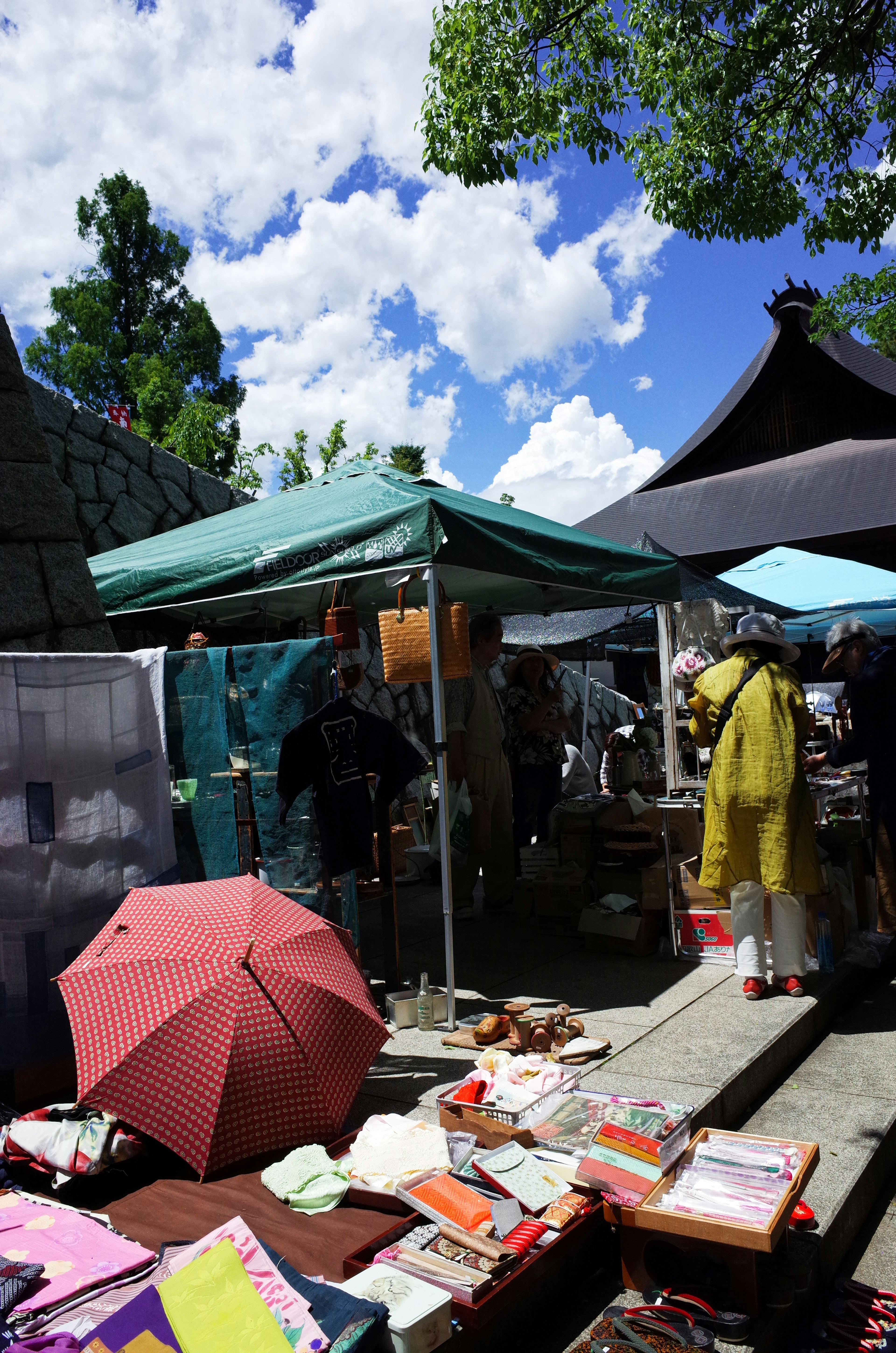 Scène de marché sous un ciel bleu avec des tentes et des parapluies colorés divers articles à vendre