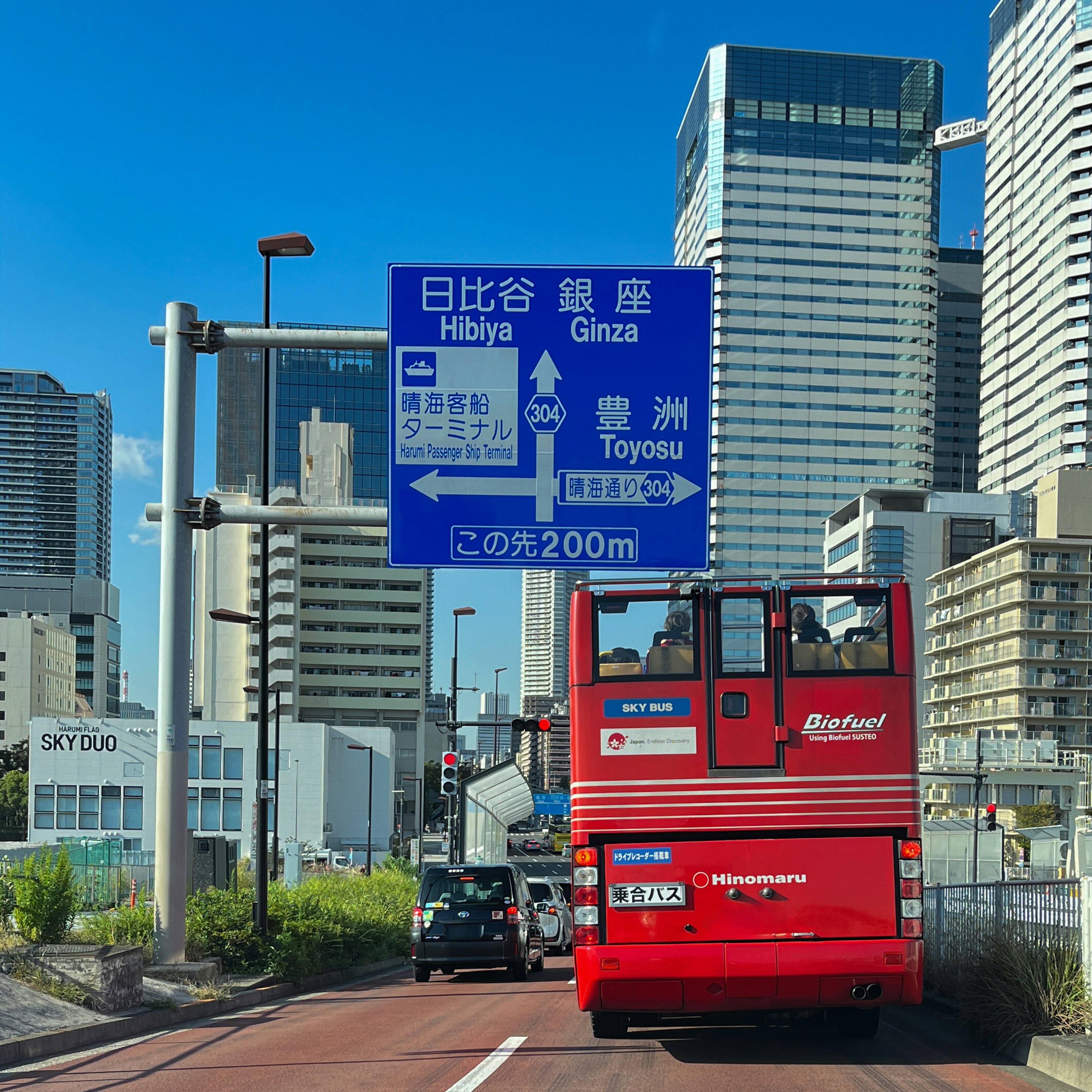 Red sightseeing bus driving on city road with skyscrapers in background