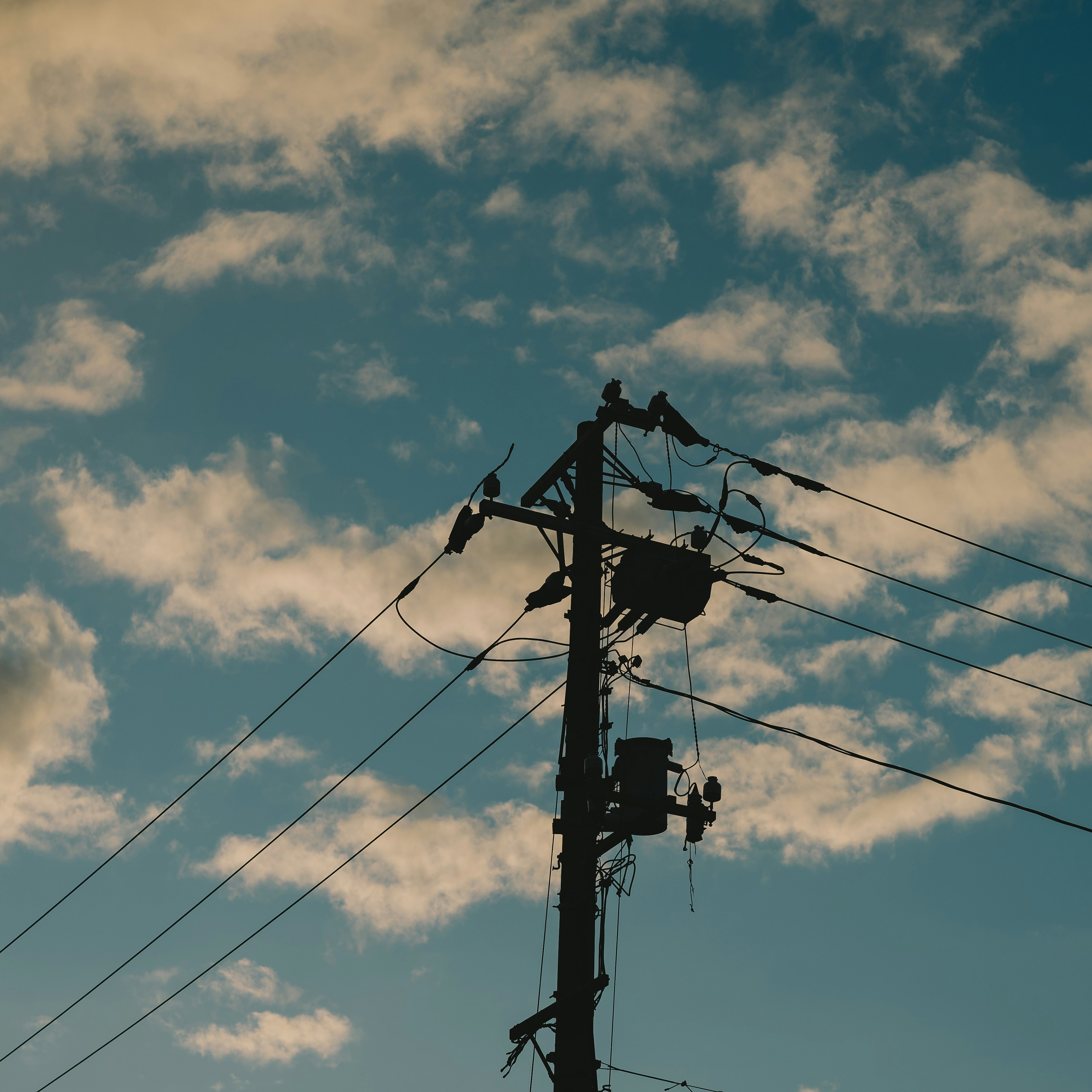 Poste de electricidad en silueta contra un cielo azul con nubes y pájaros