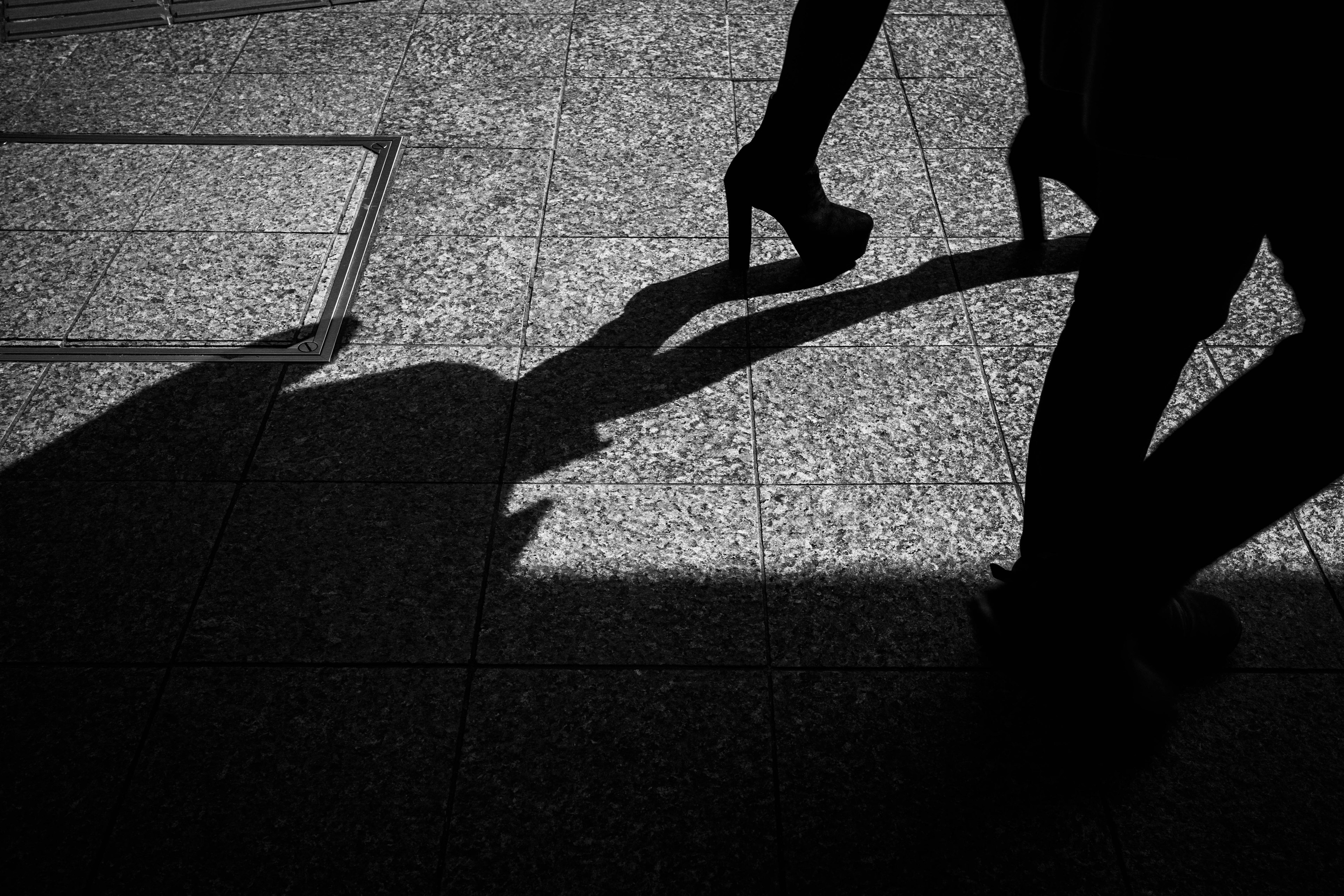 Black and white photo of a person's shadow wearing high heels on pavement