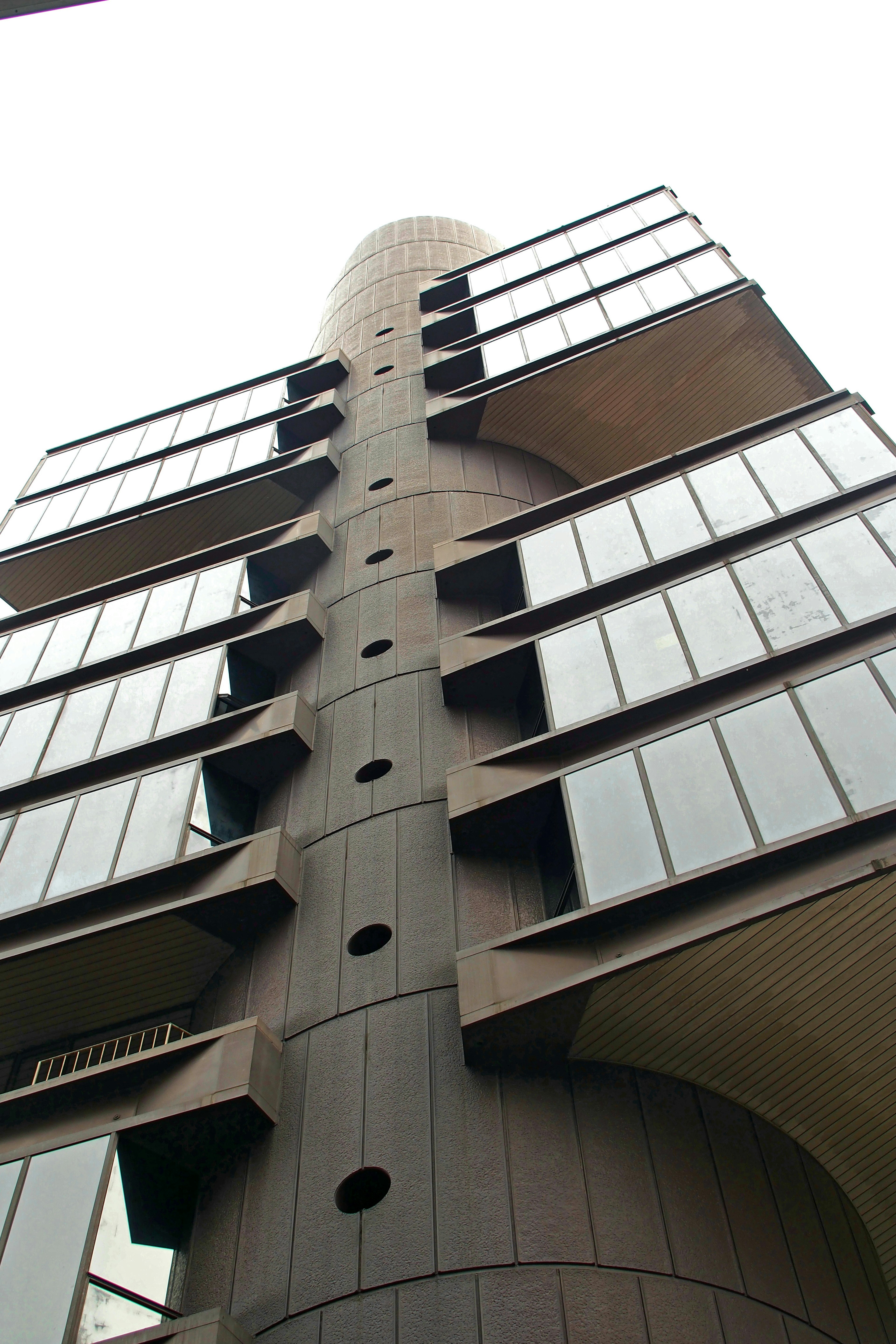 View of a tall building from below showcasing unique windows and curved design