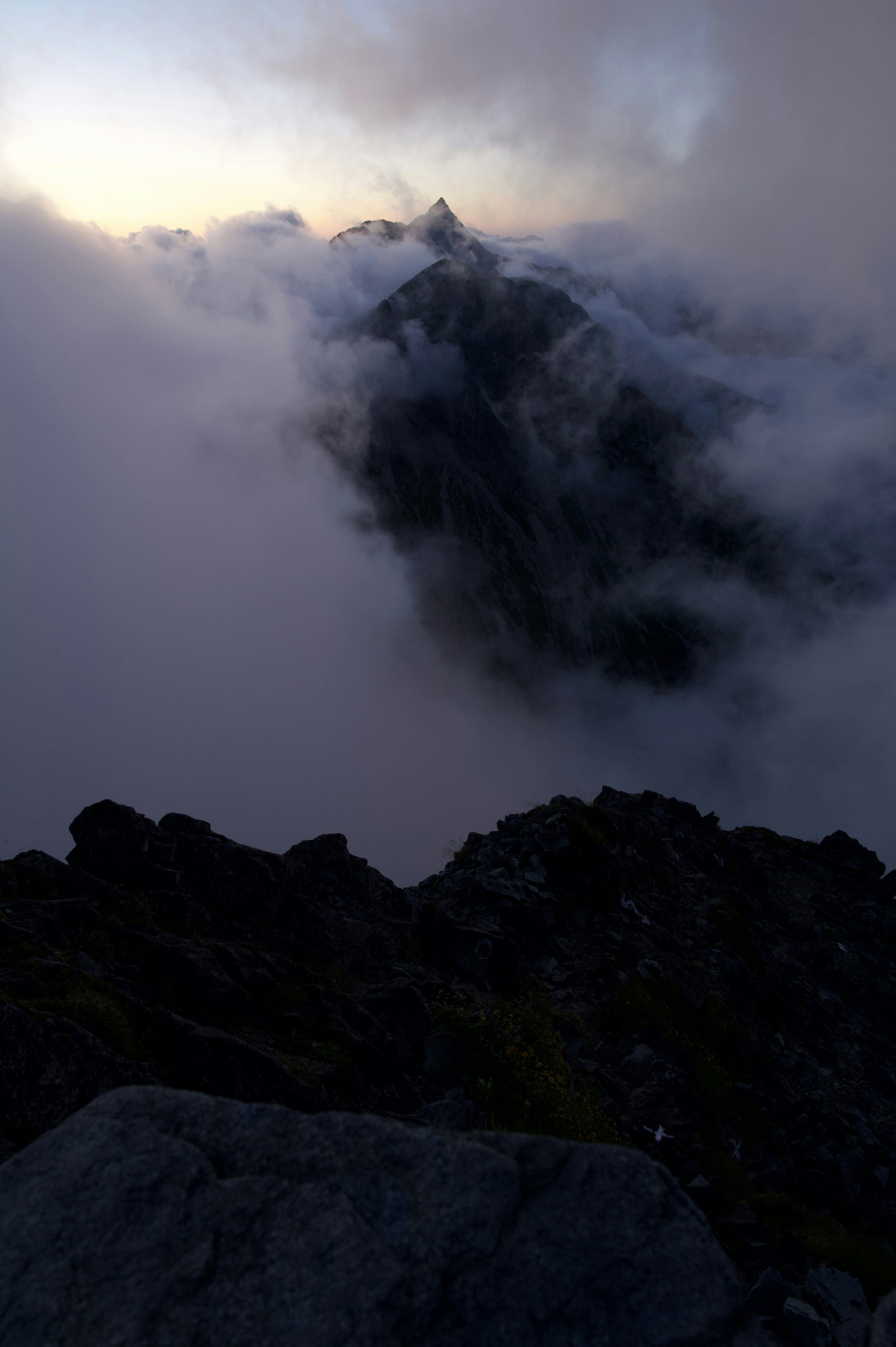 Mountain peak emerging from fog with rocky foreground