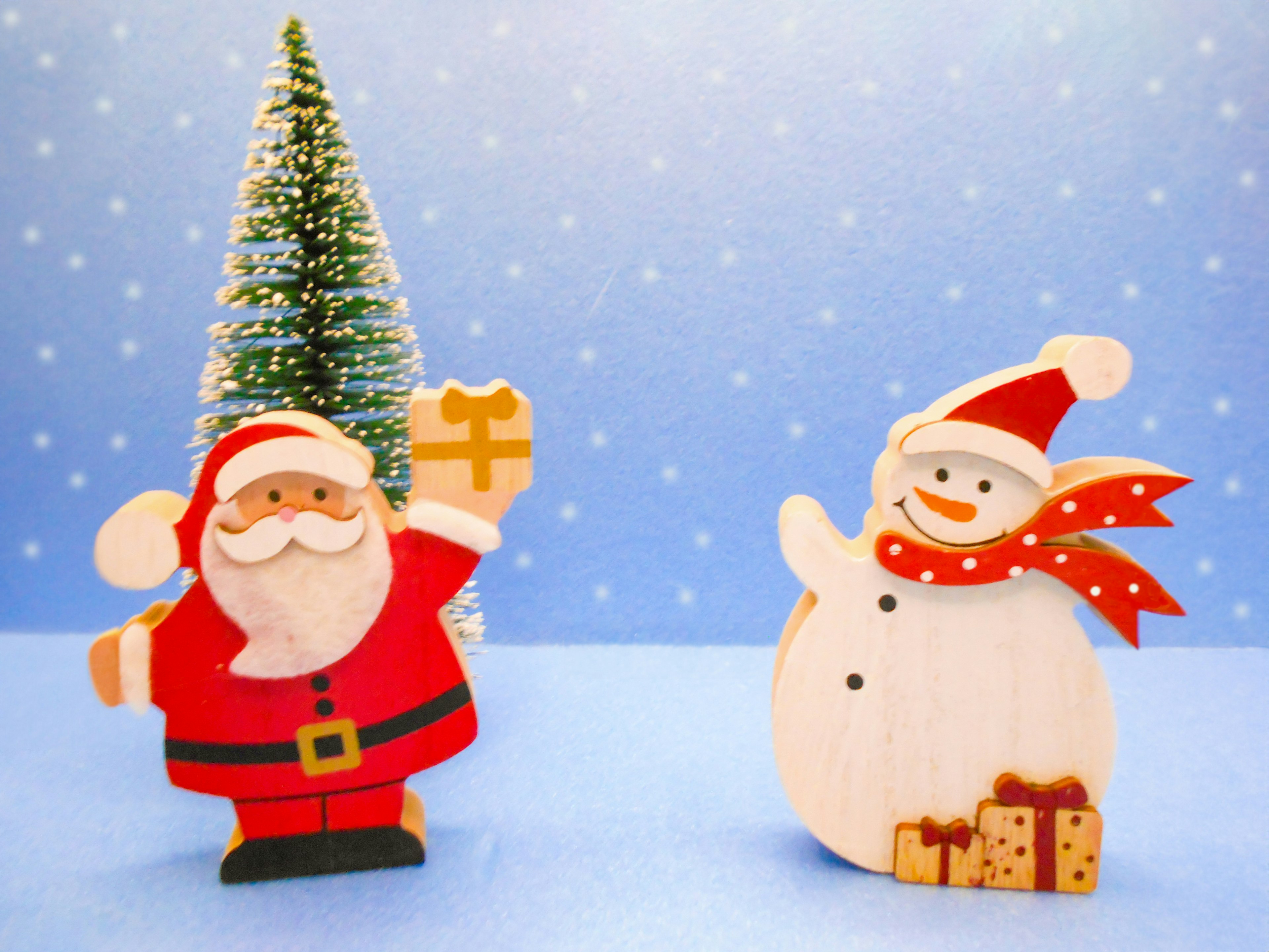 Wooden decorations of Santa Claus and a snowman standing in front of a blue background