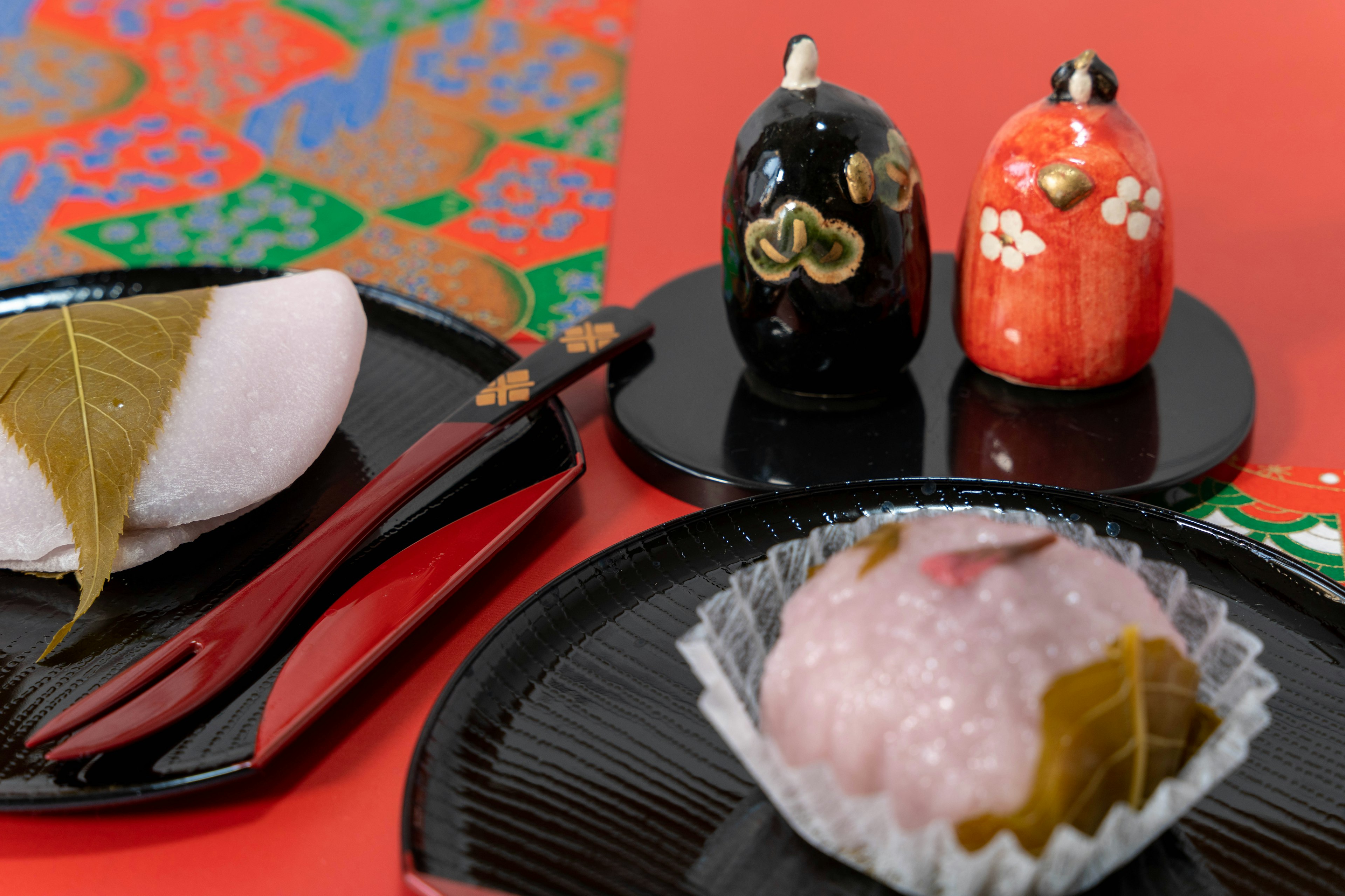 Beautiful table setting with Japanese sweets and traditional ornaments on a red background