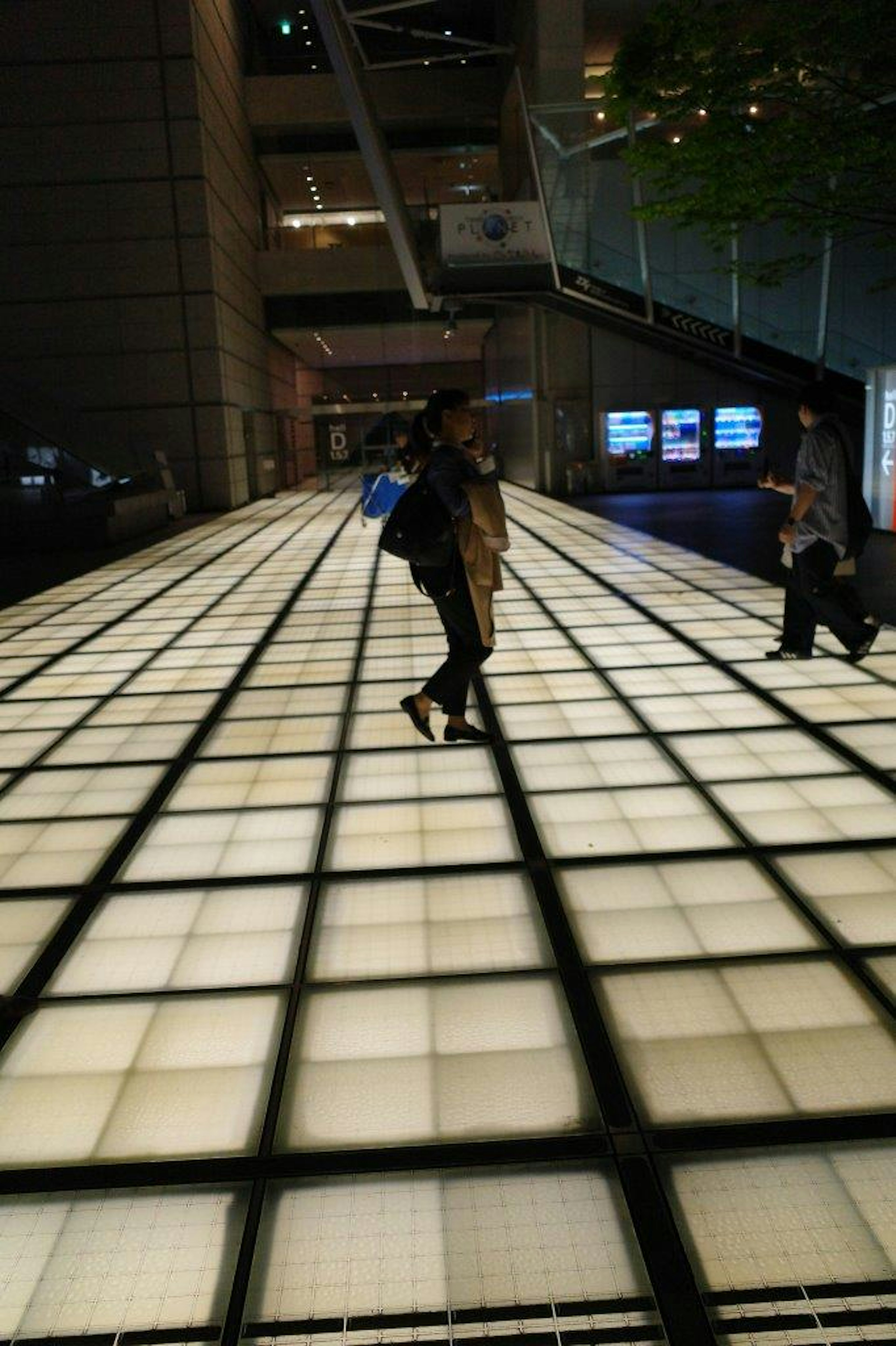 People walking on a brightly lit tiled floor at night