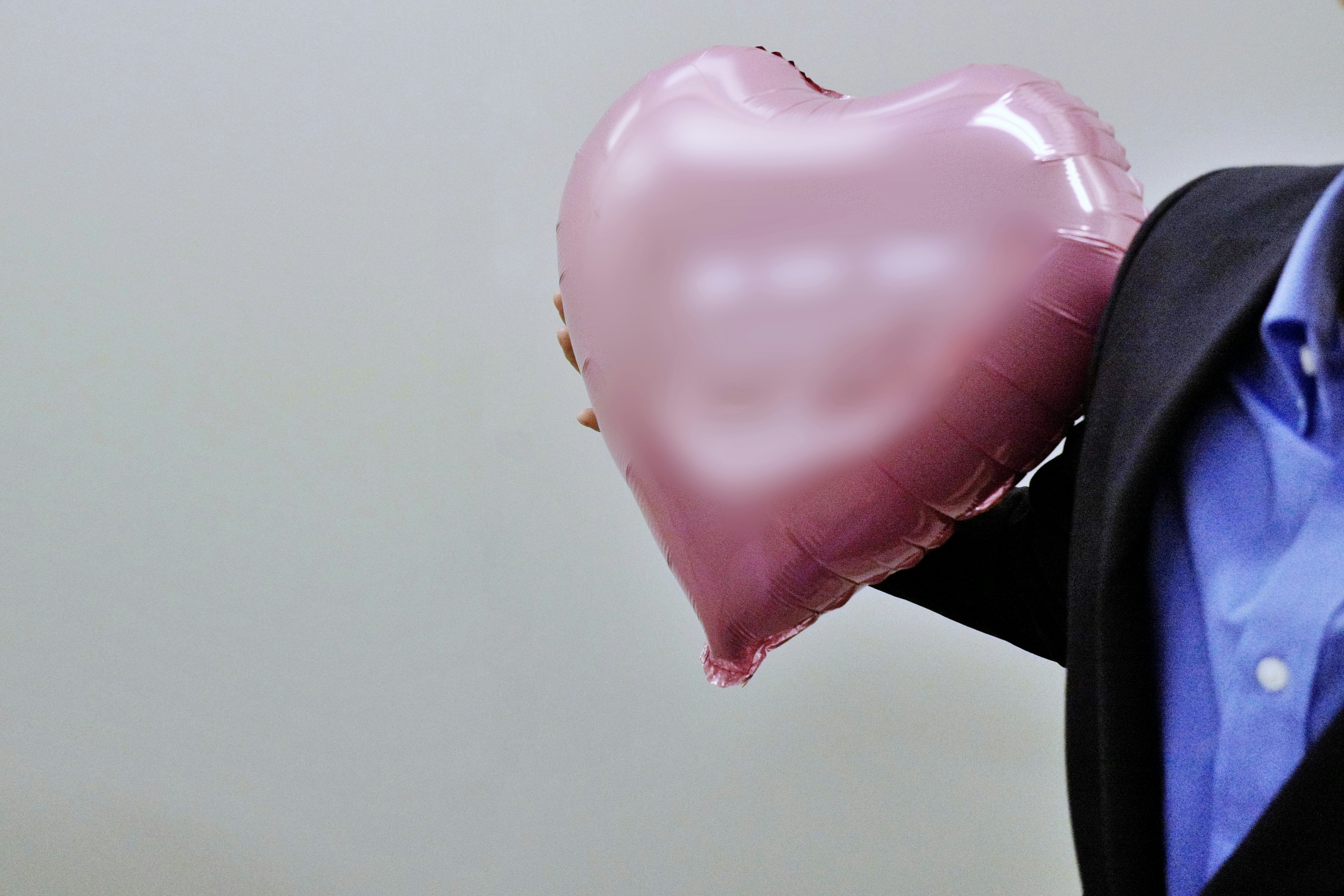 Hombre con traje sosteniendo un globo en forma de corazón rosa