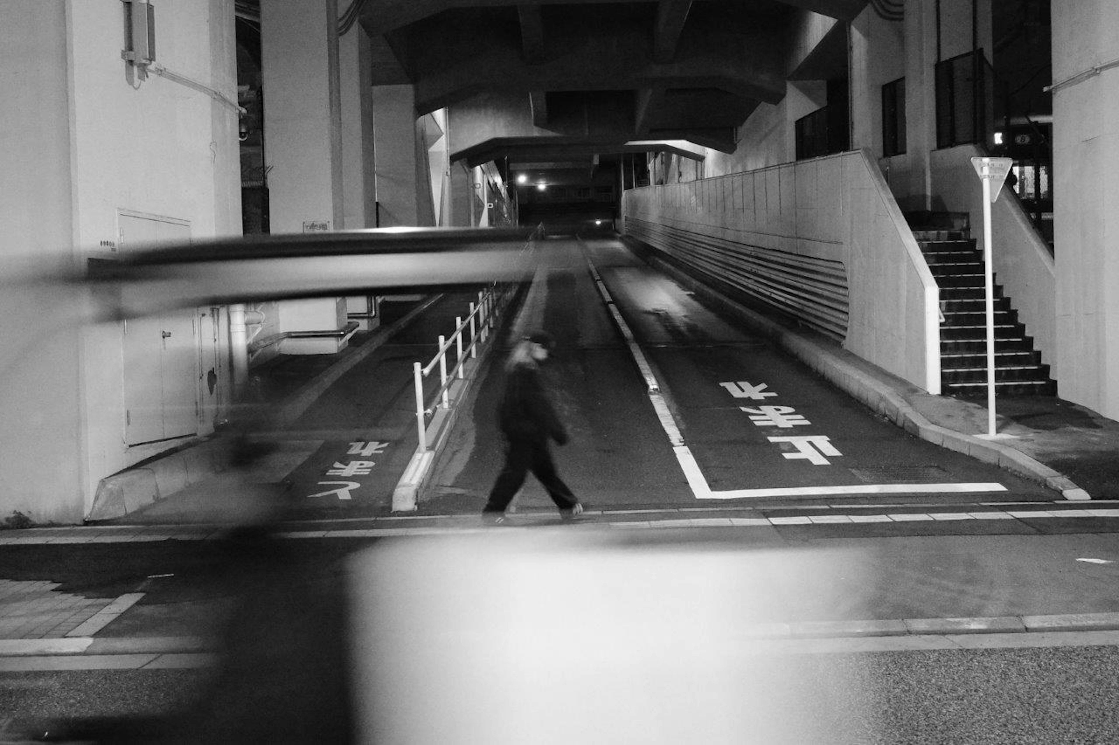 Black and white photo of a pedestrian crossing the street in a nighttime city