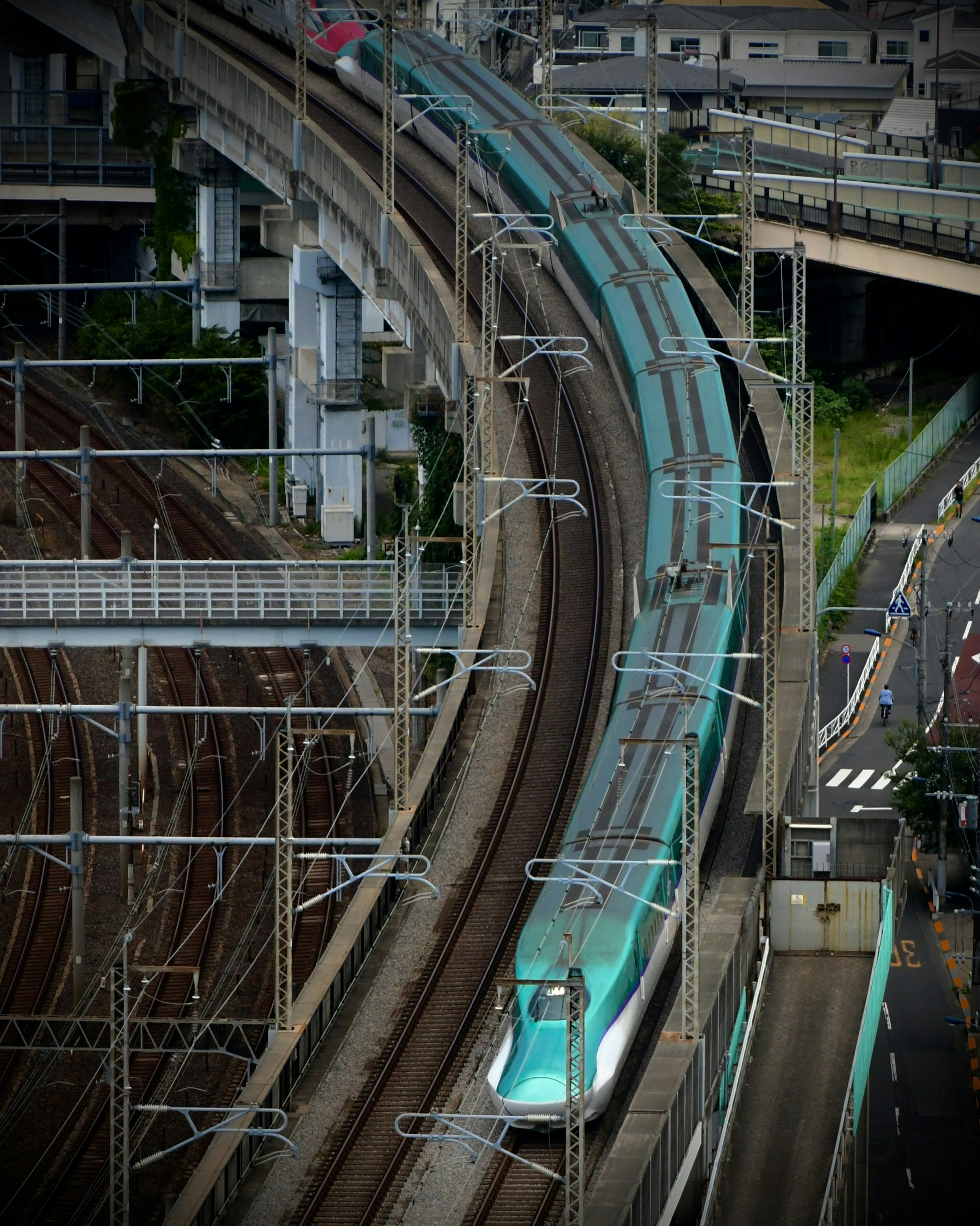 Green Shinkansen train traveling on curved tracks in an urban setting