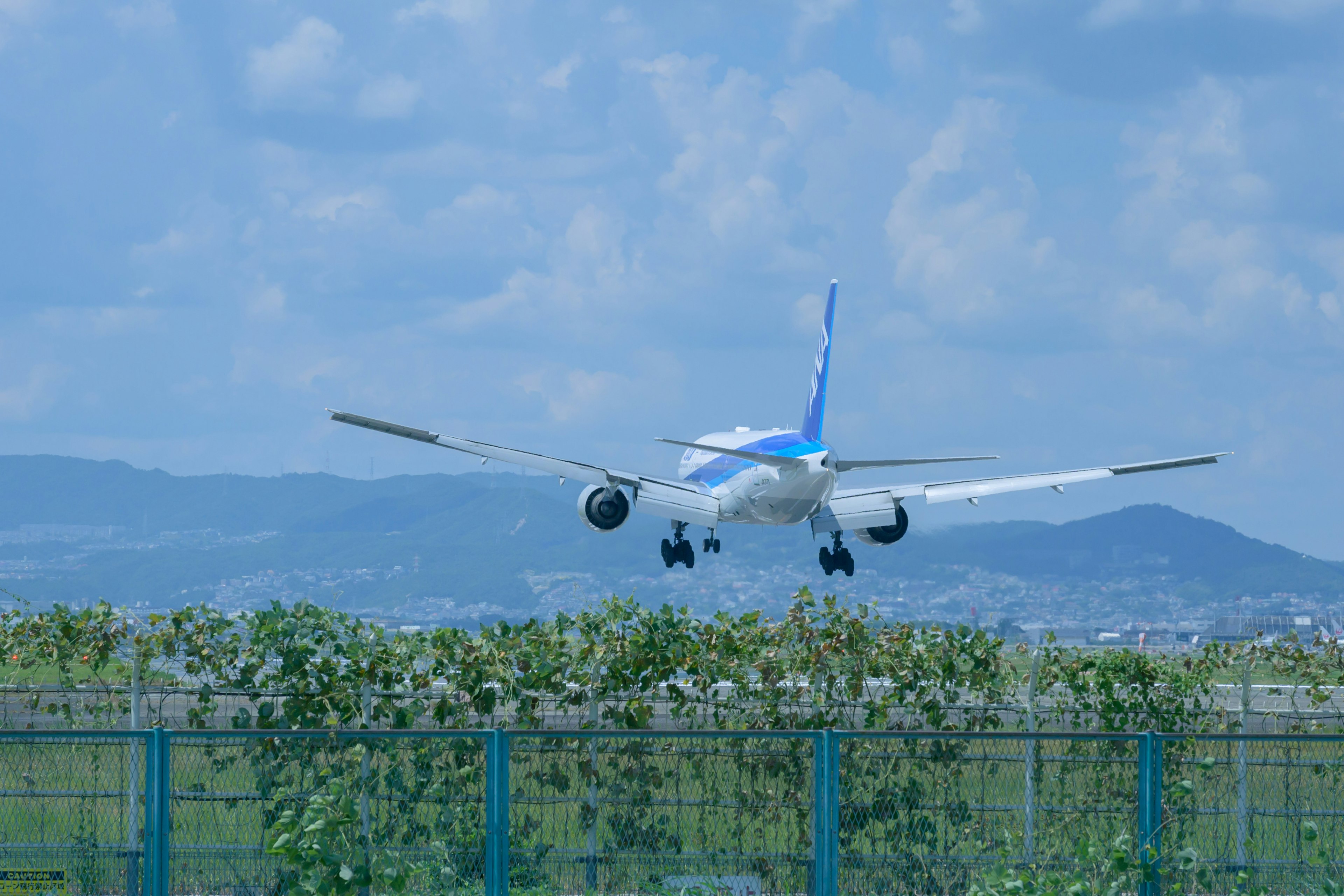 Airplane landing under a blue sky with green fence in the foreground