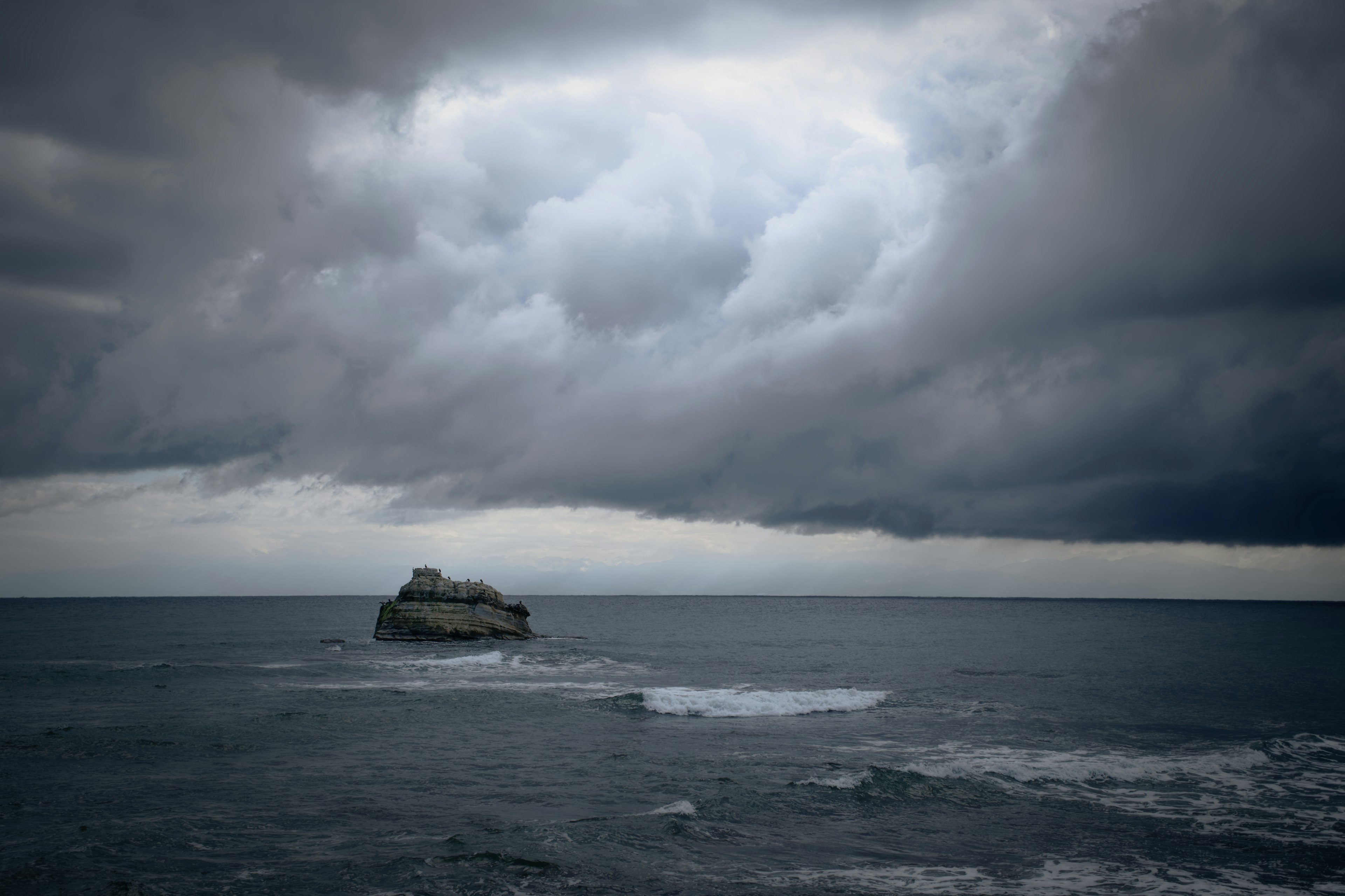 Batu terisolasi di bawah awan gelap di atas laut