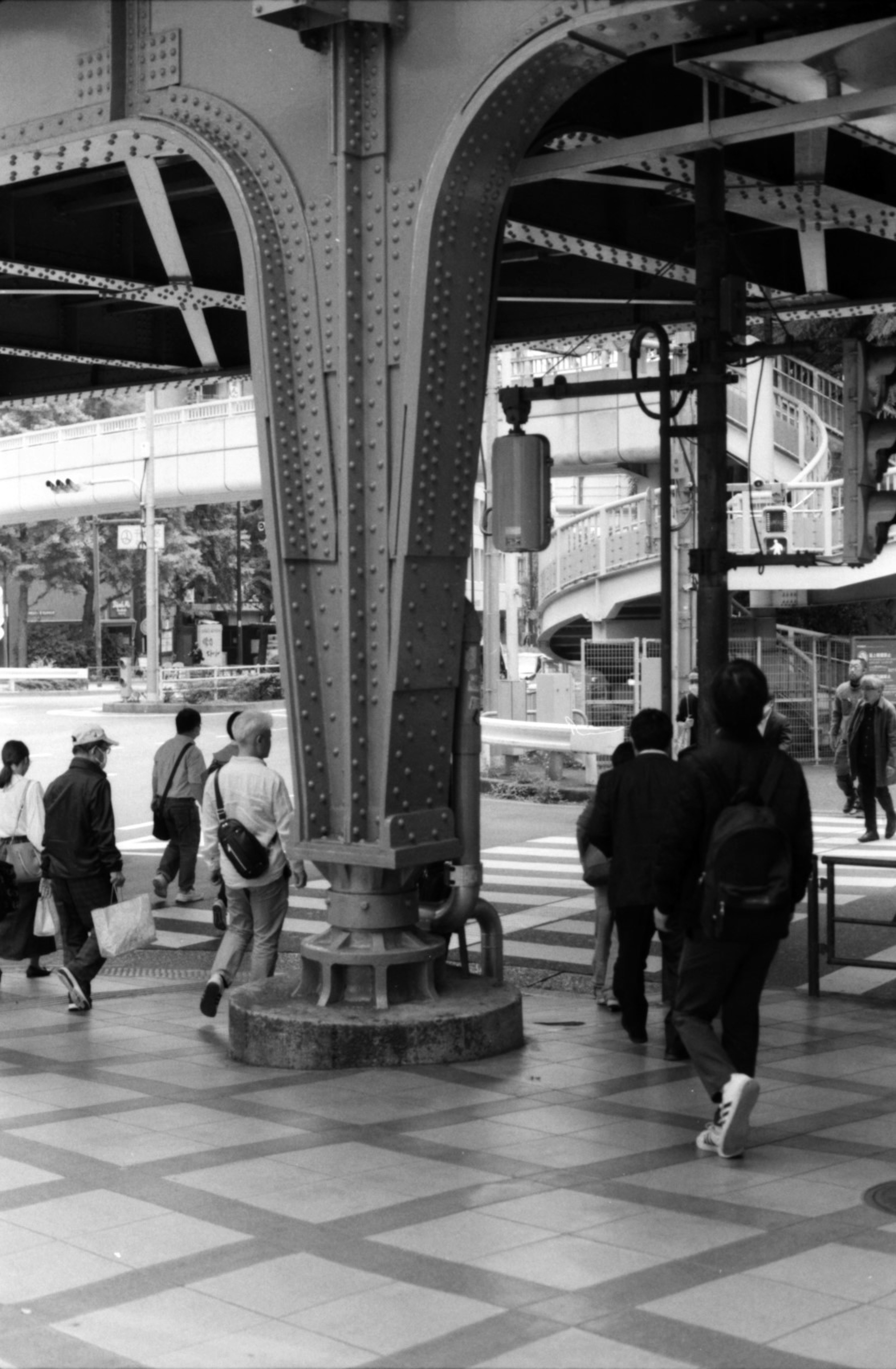 Black and white urban scene featuring a metal column with people walking by