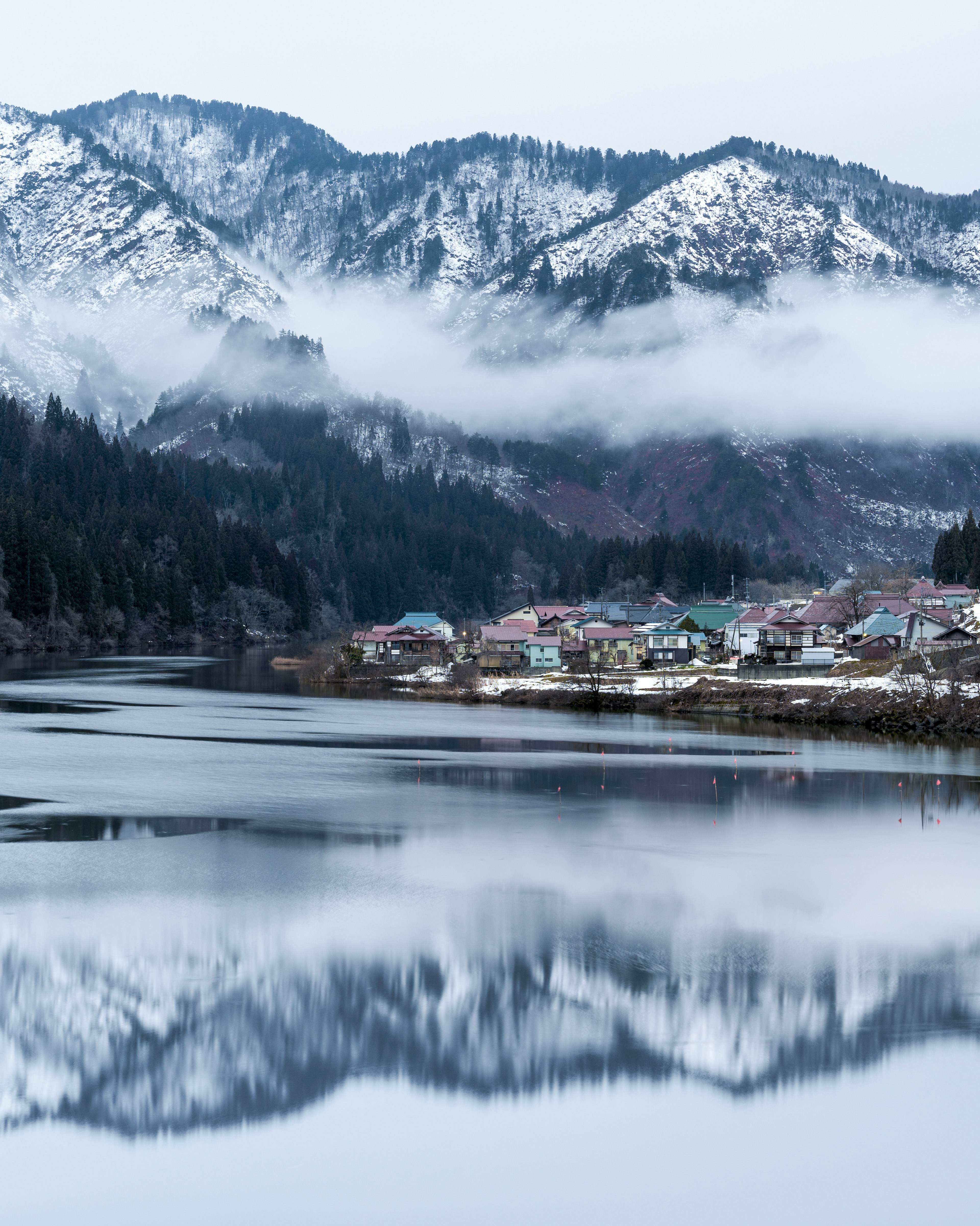 Snow-covered mountains and serene lake landscape reflecting village houses and mist