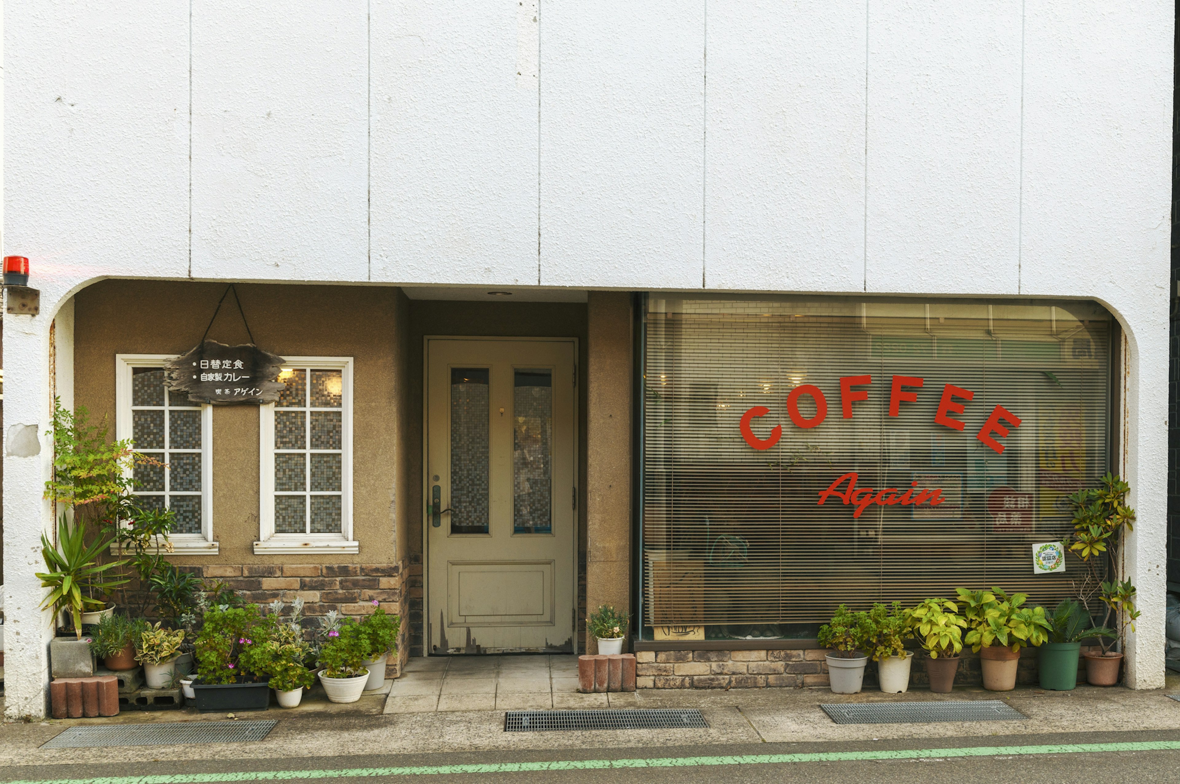 Exterior de una cafetería con plantas verdes a lo largo de la entrada