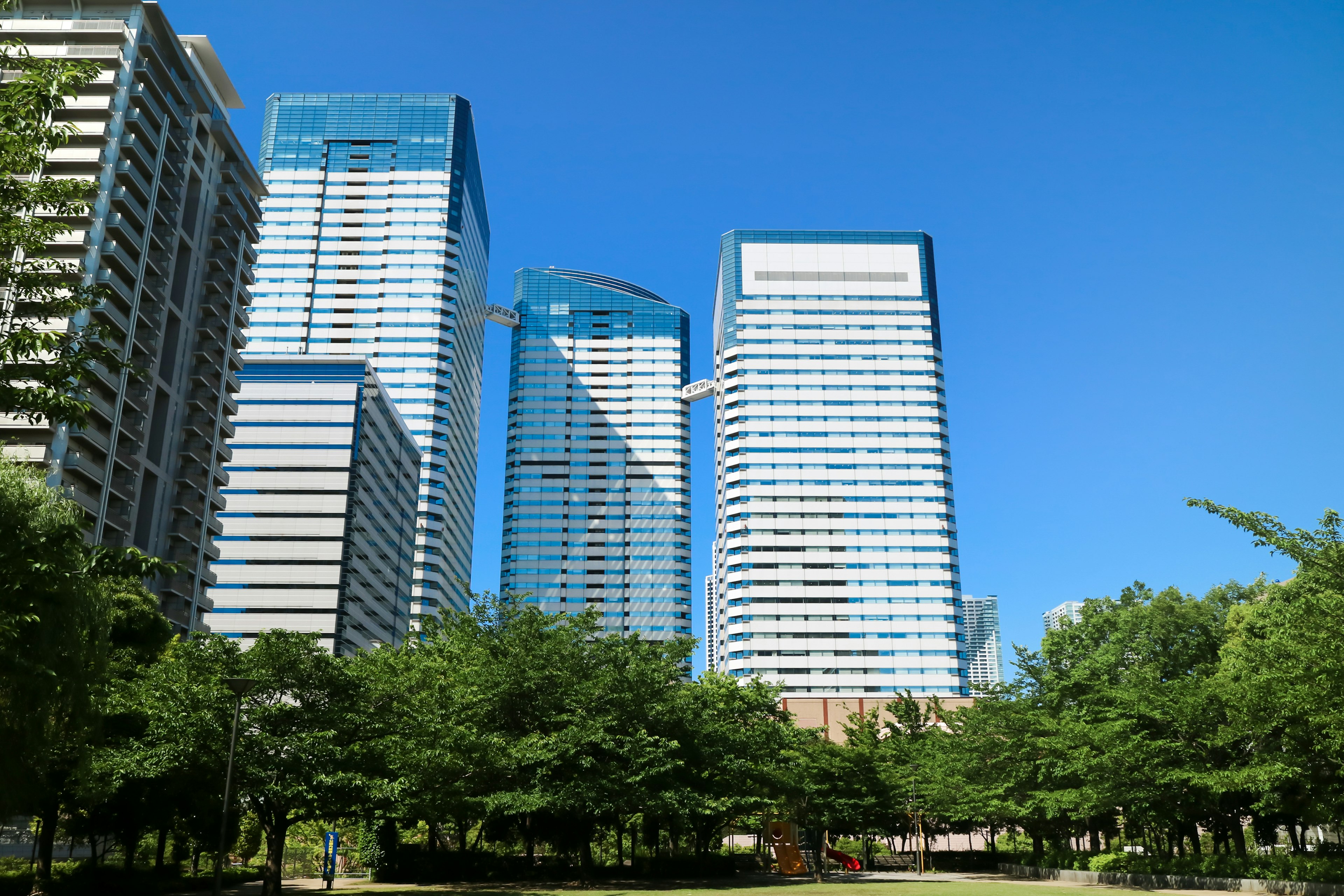 Una vista de altos edificios contra un cielo azul claro con árboles verdes en primer plano