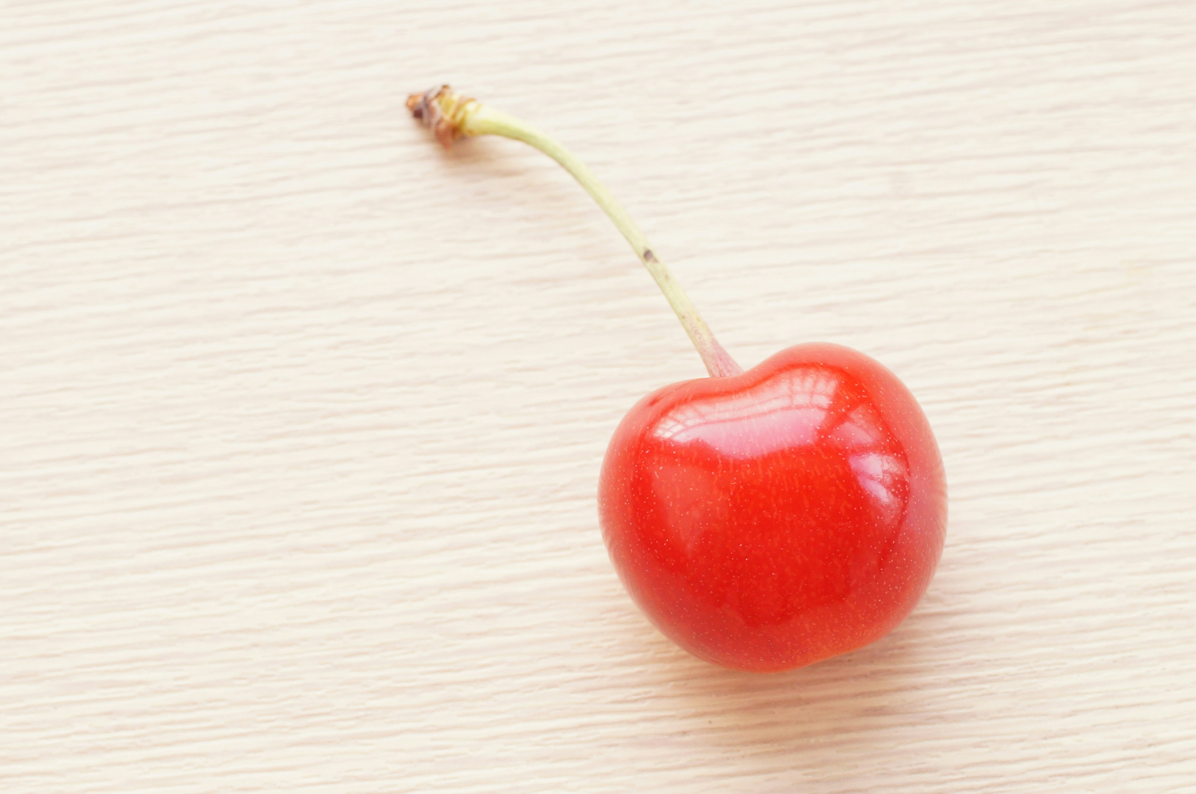 A vibrant red cherry resting on a simple wooden table