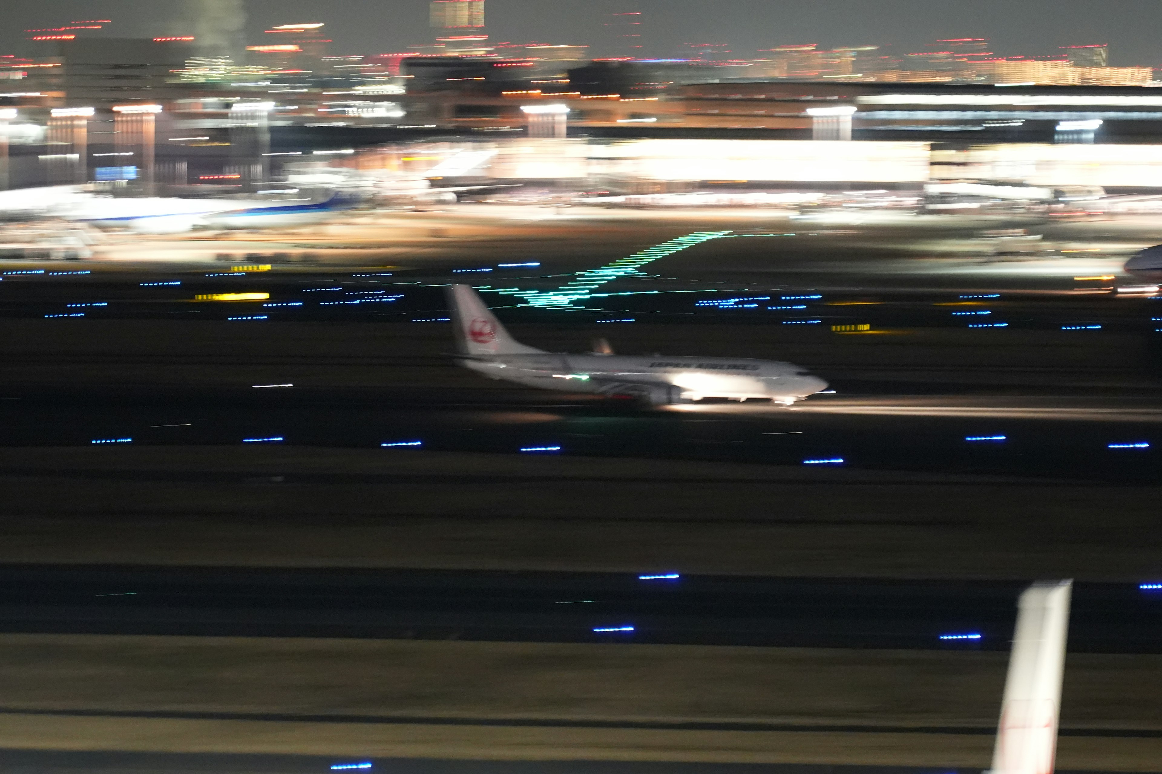 Un avión rodando por una pista de noche con luces de la ciudad borrosas de fondo