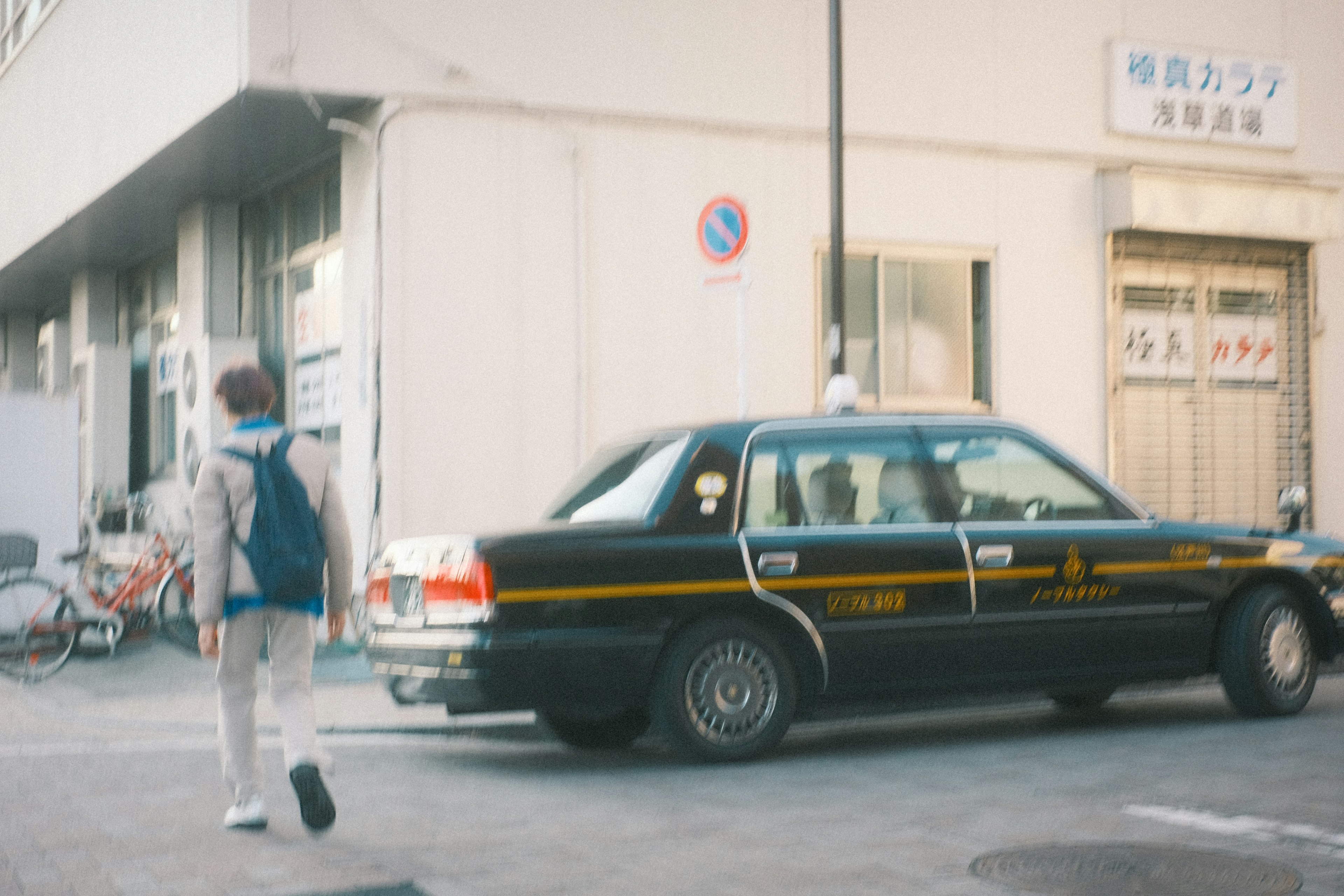 A person walking near a parked black taxi on a street corner