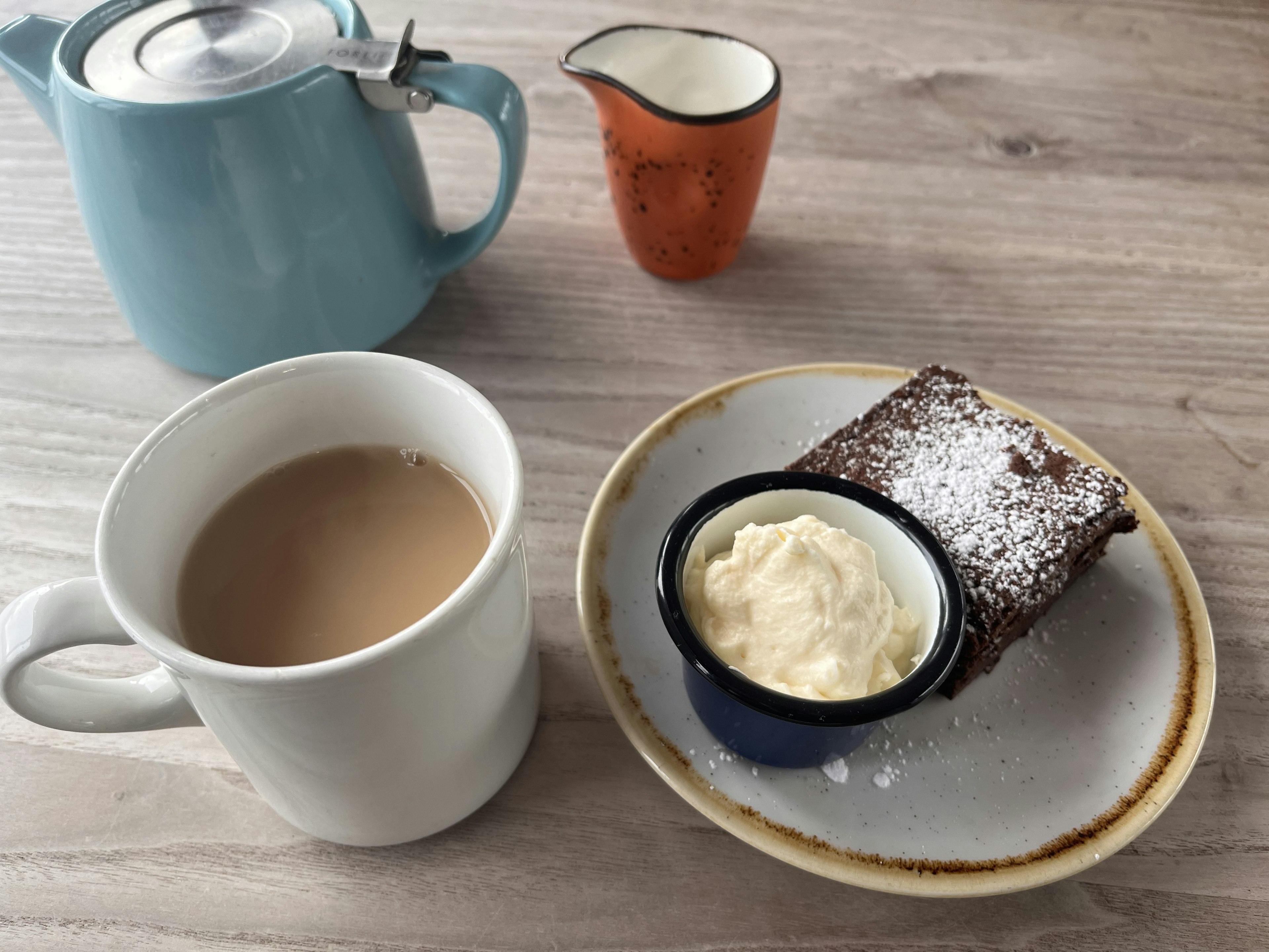 青いティーポットとカップに入った紅茶とデザートの皿にクリームが盛られたチョコレートケーキ