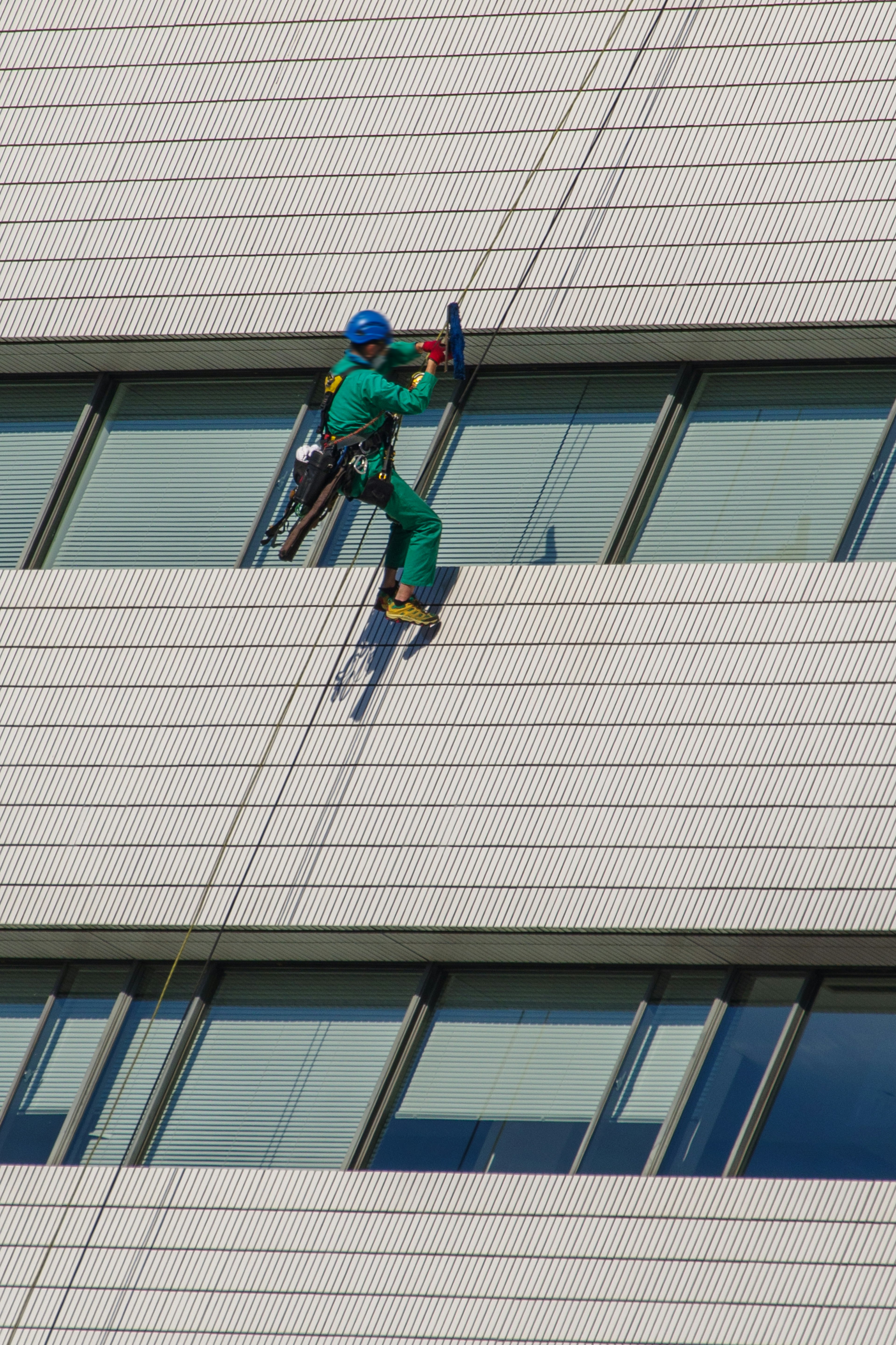 Lavoratore che scala la facciata di un edificio indossando abiti da lavoro verdi e un casco