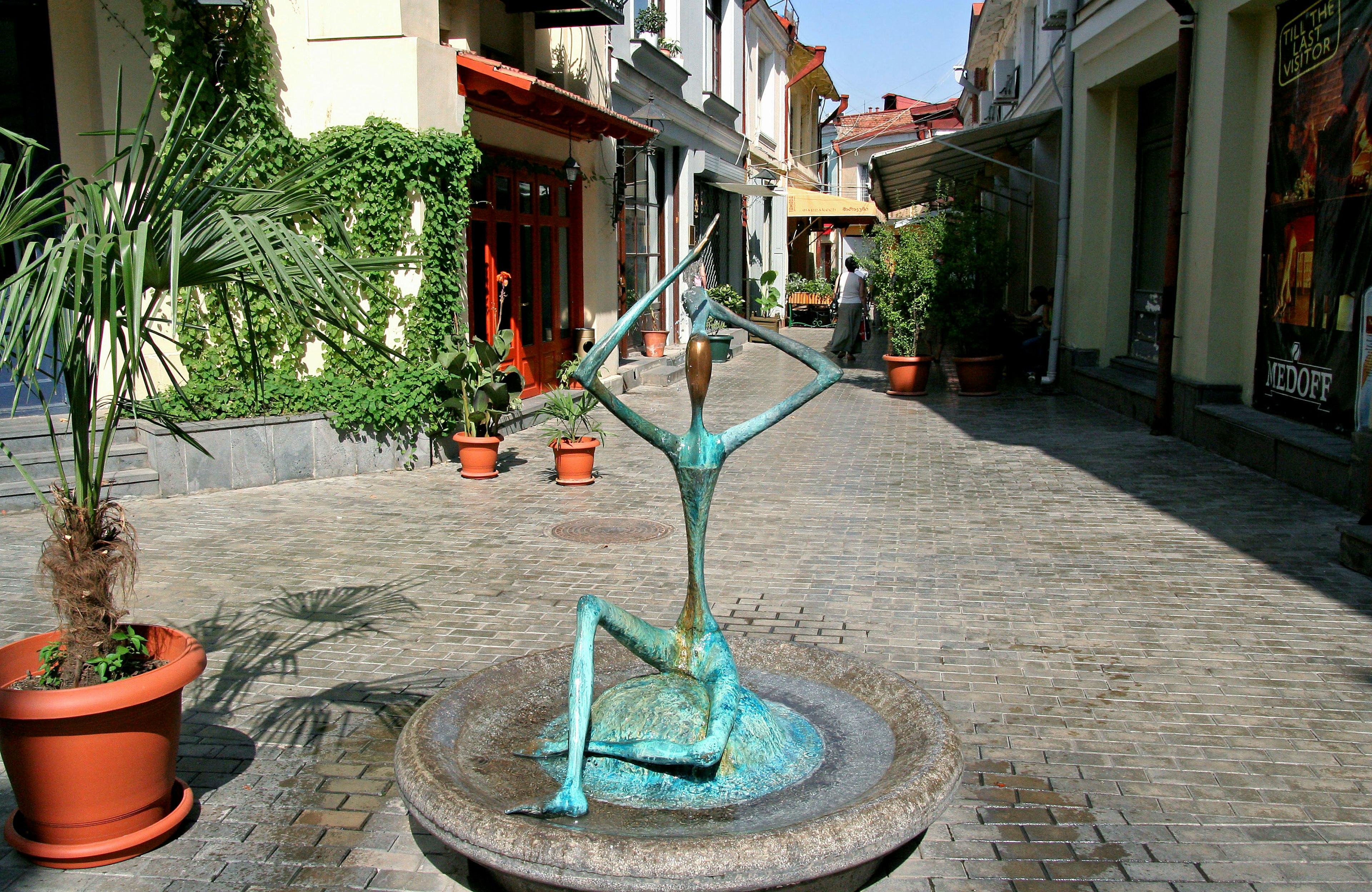 Sculpture en bronze dans une rue pavée avec des magasins et des plantes en pot