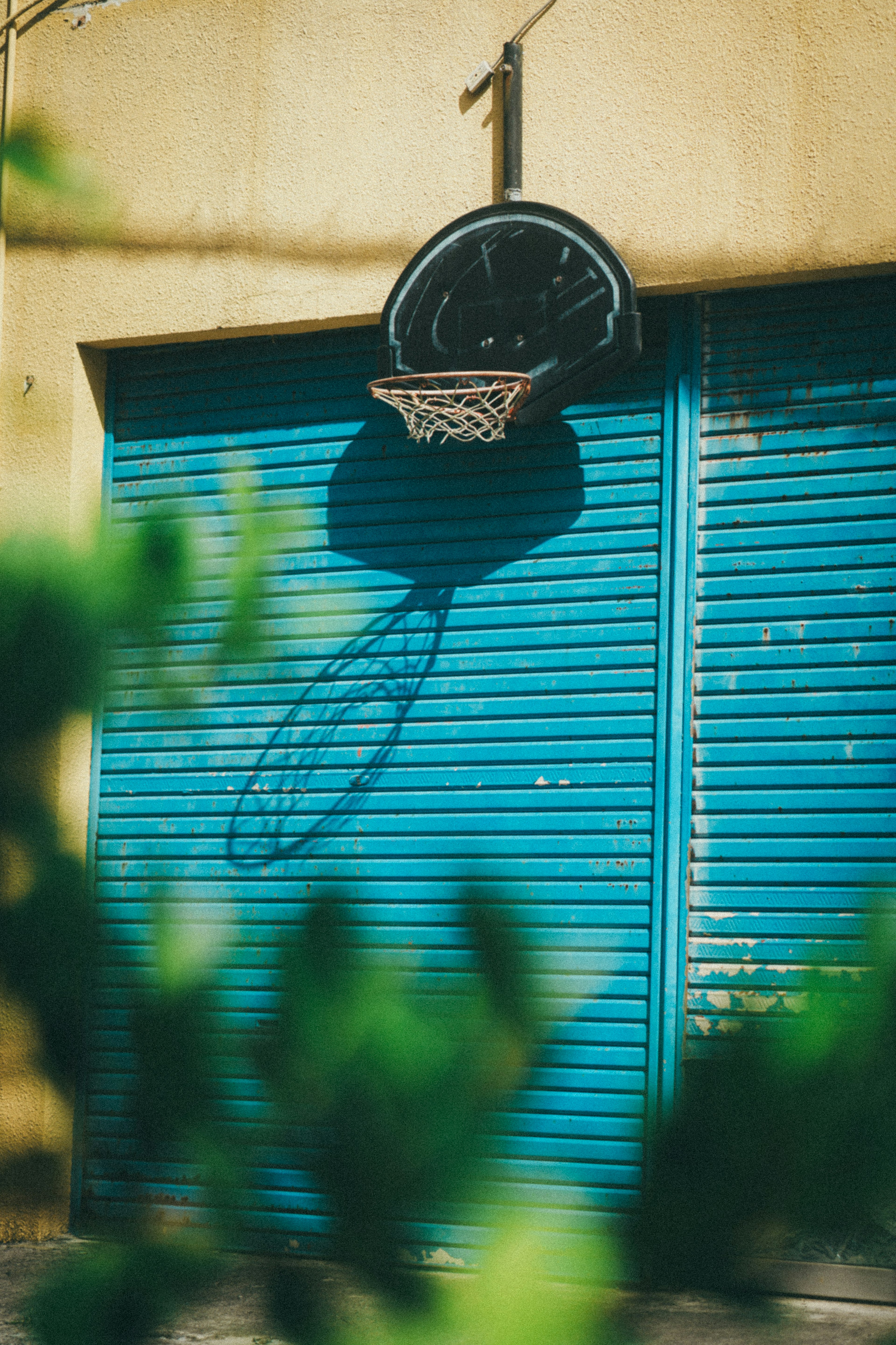 Basketball hoop mounted on a wall with a shadow cast on a blue shutter