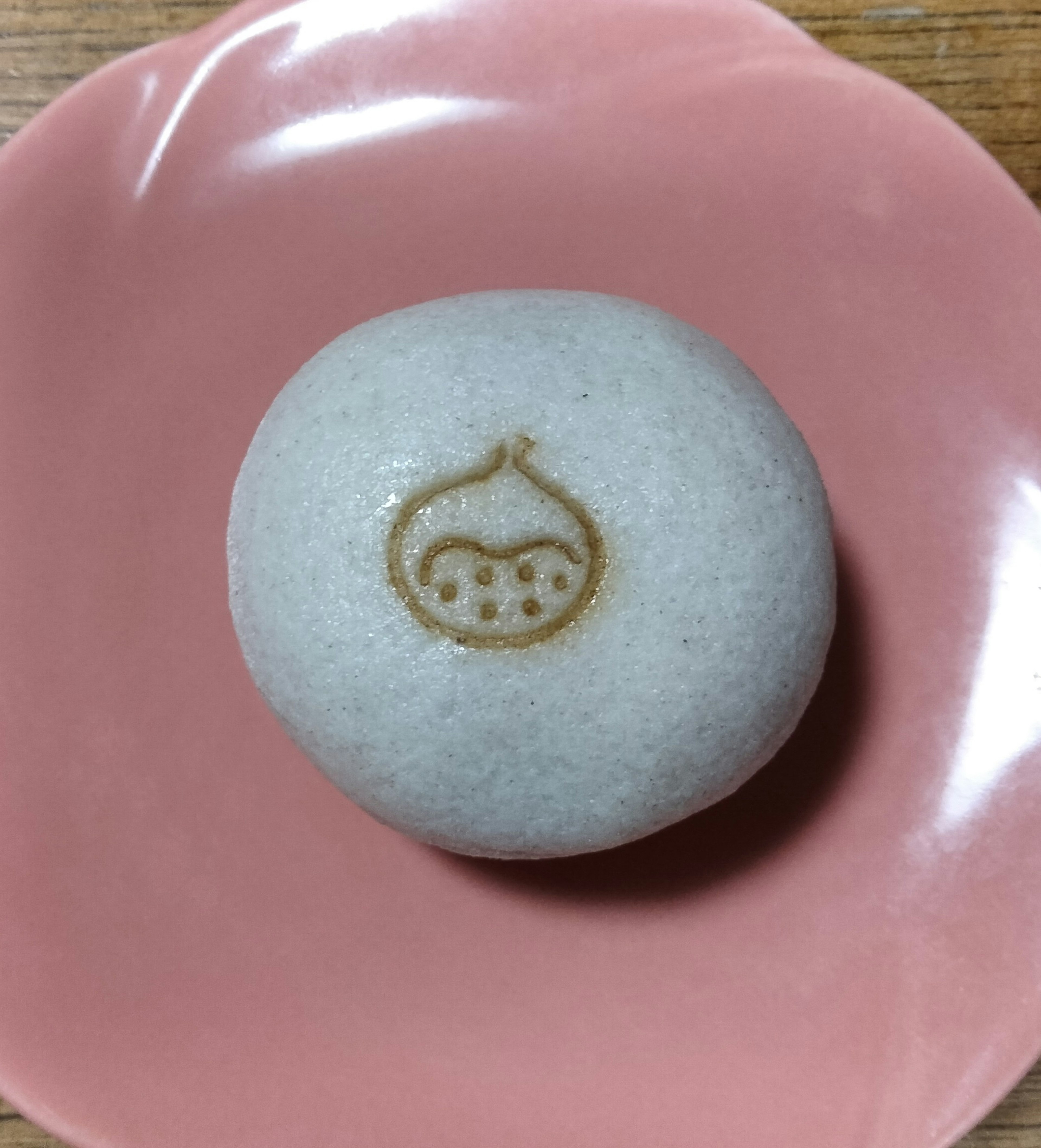 A round white Japanese dessert placed on a pink plate featuring a chestnut design