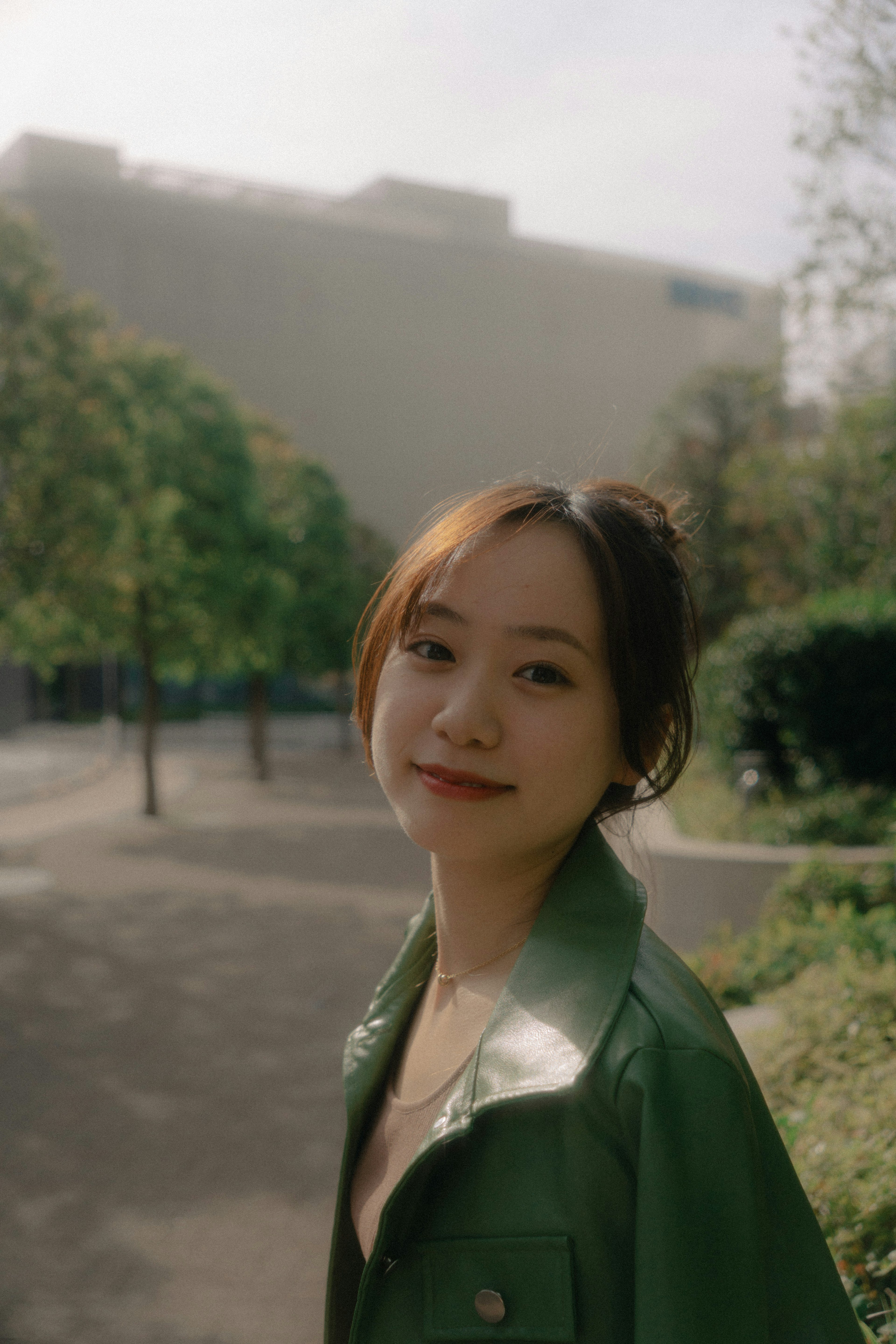 A woman in a green jacket smiling in a park setting