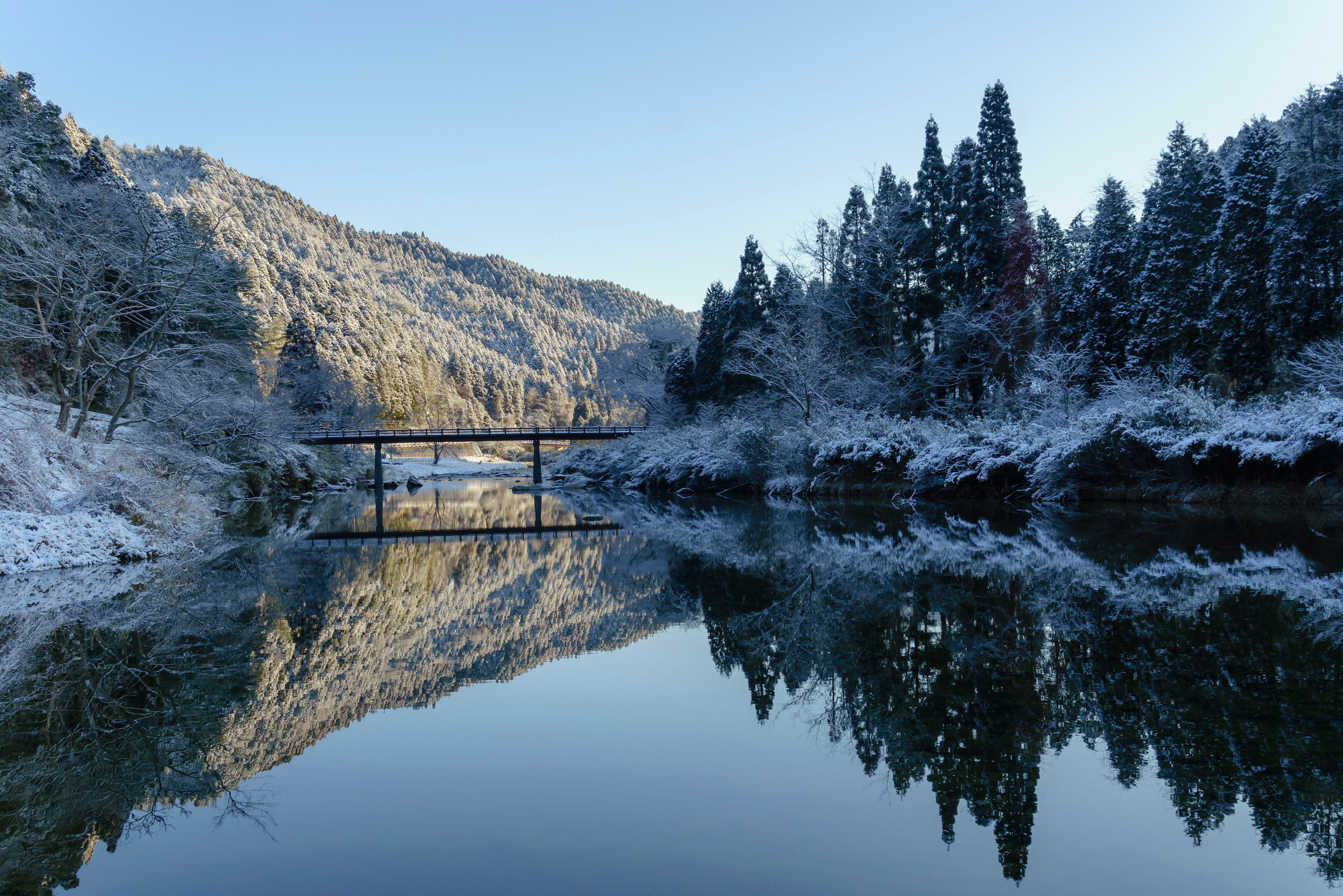 Winterlandschaft mit schneebedeckten Bergen und der Reflexion eines ruhigen Flusses