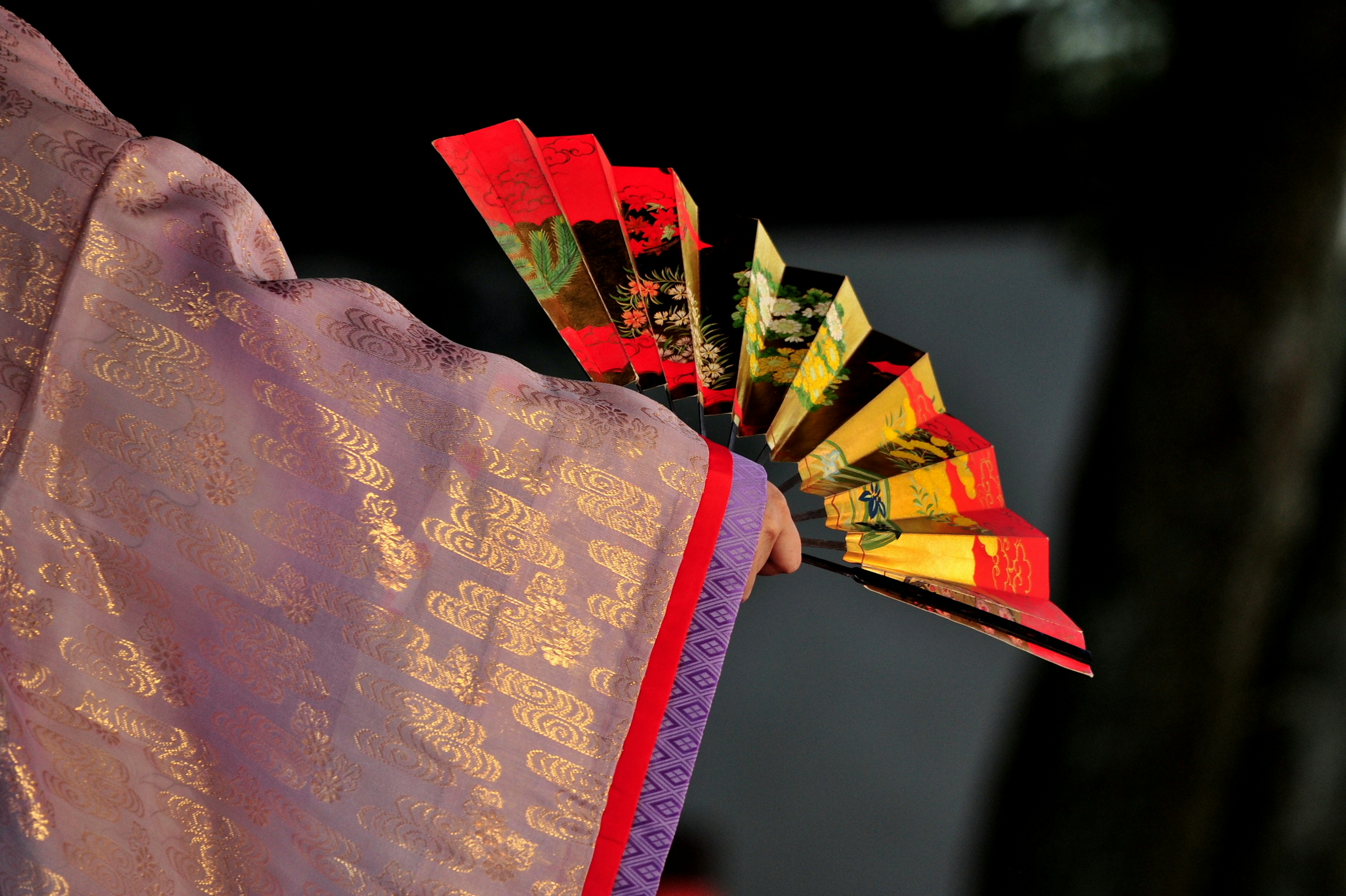 A vibrant fan held by a person in a purple kimono