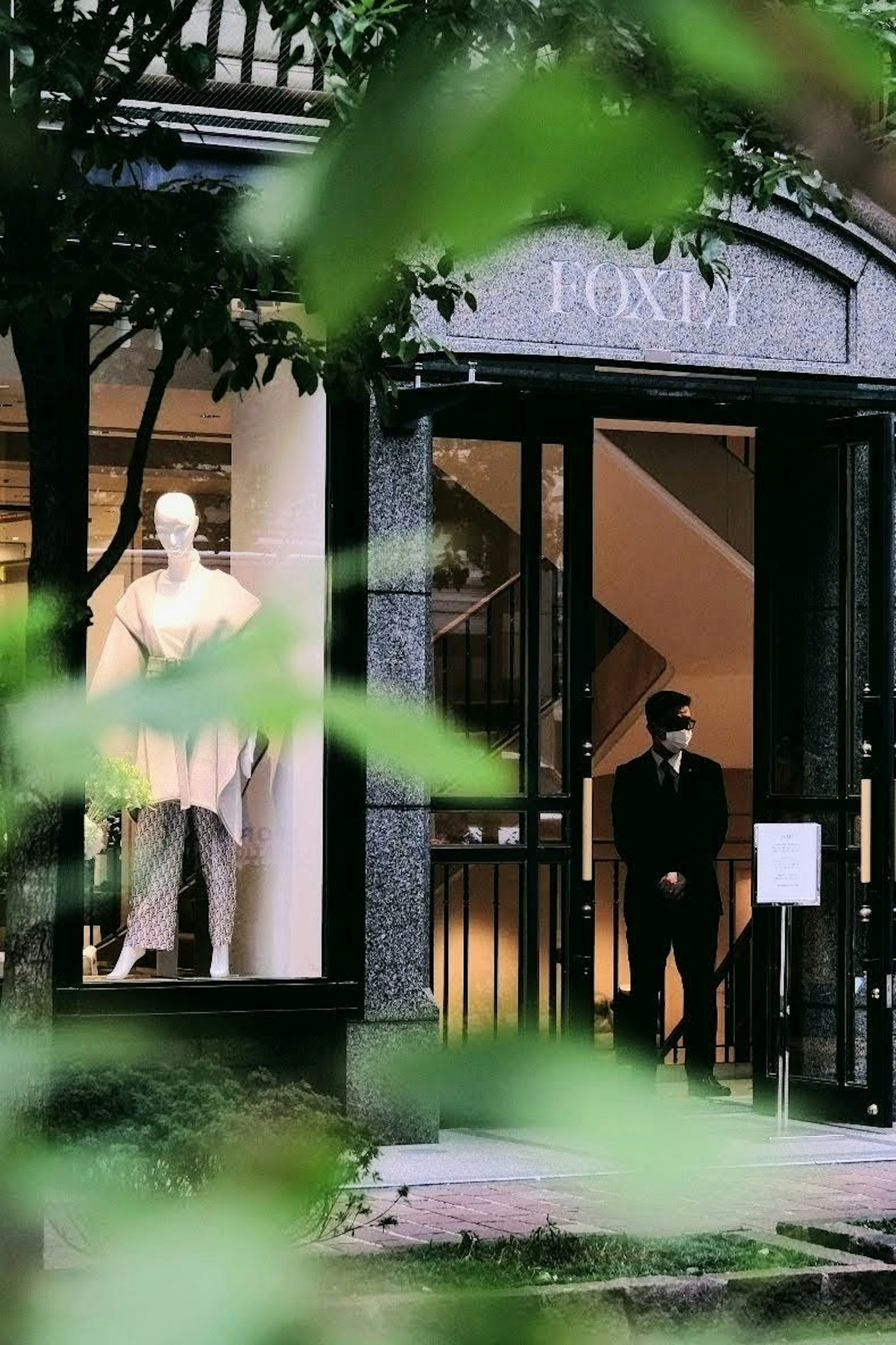 Un hombre de pie en la entrada de una tienda de moda de lujo con un maniquí en la ventana