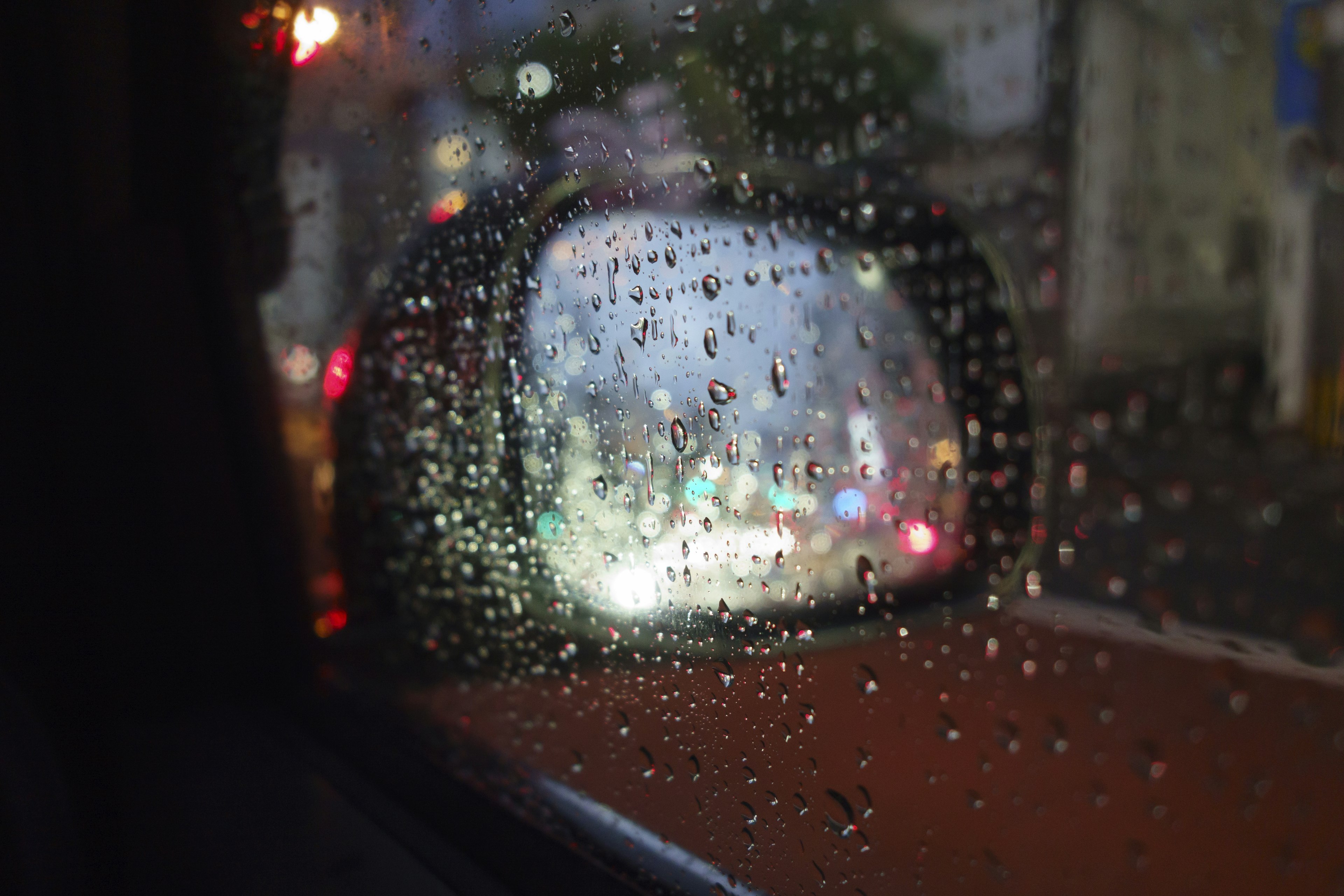 Close-up of a side mirror with raindrops viewed from inside a car