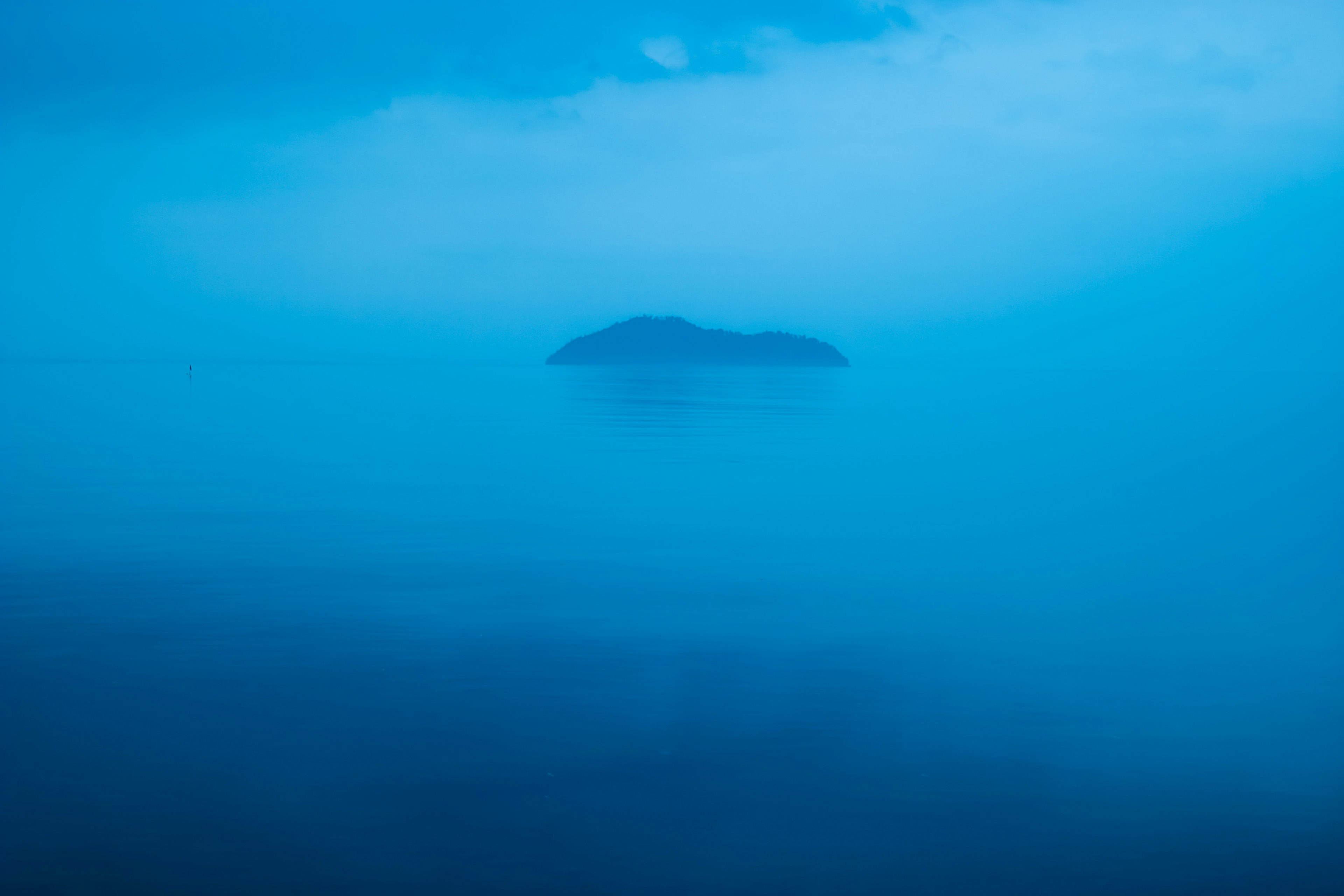 Un paisaje marino tranquilo con una pequeña isla envuelta en niebla azul