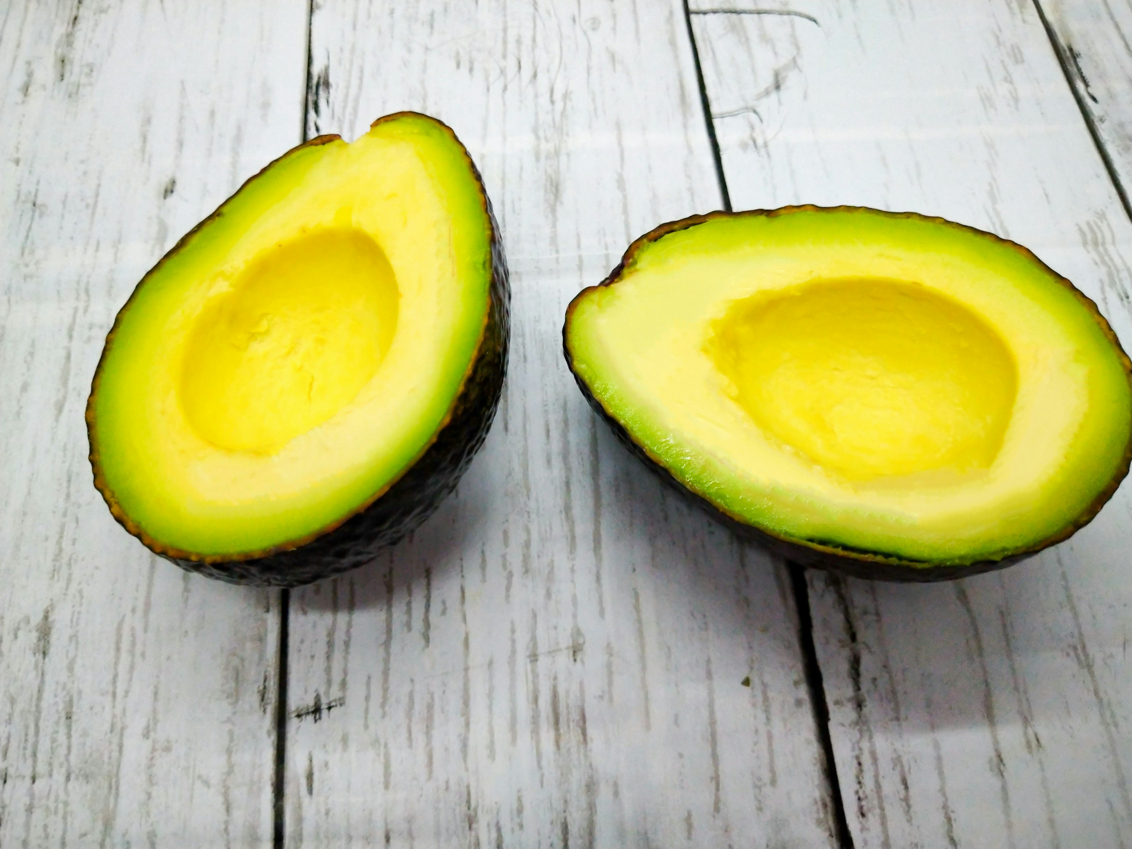 Two halves of an avocado with bright yellow flesh and green skin