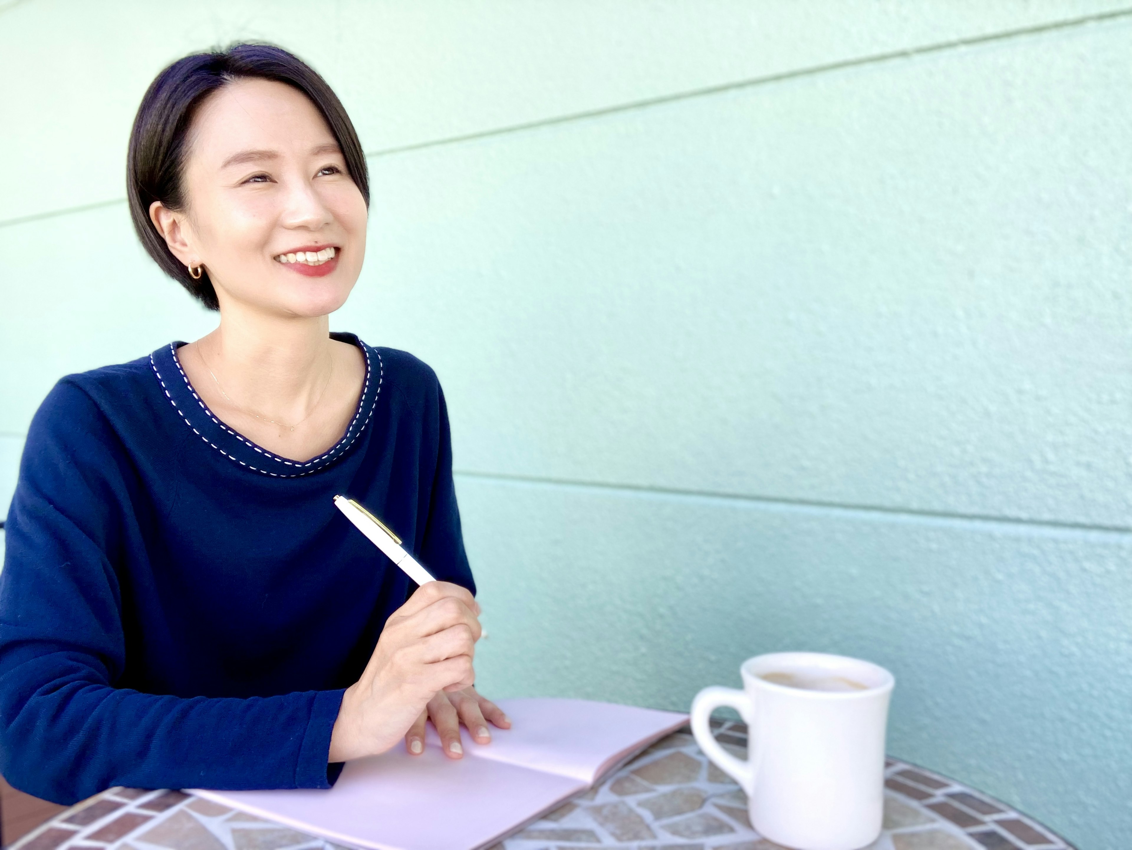 A smiling woman in a blue sweater writing in a notebook