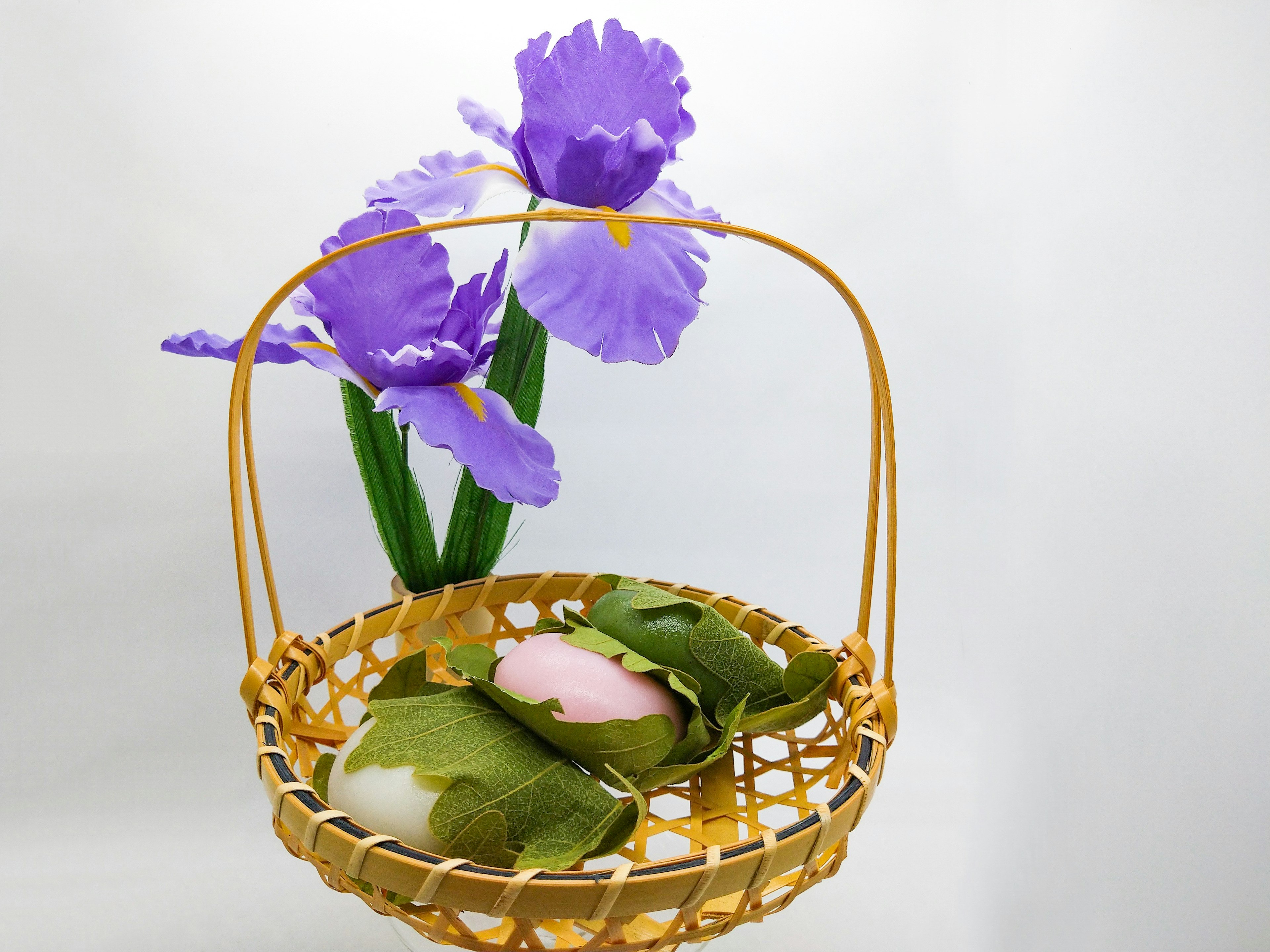 A basket with purple flowers and green leaves containing colorful rice cakes