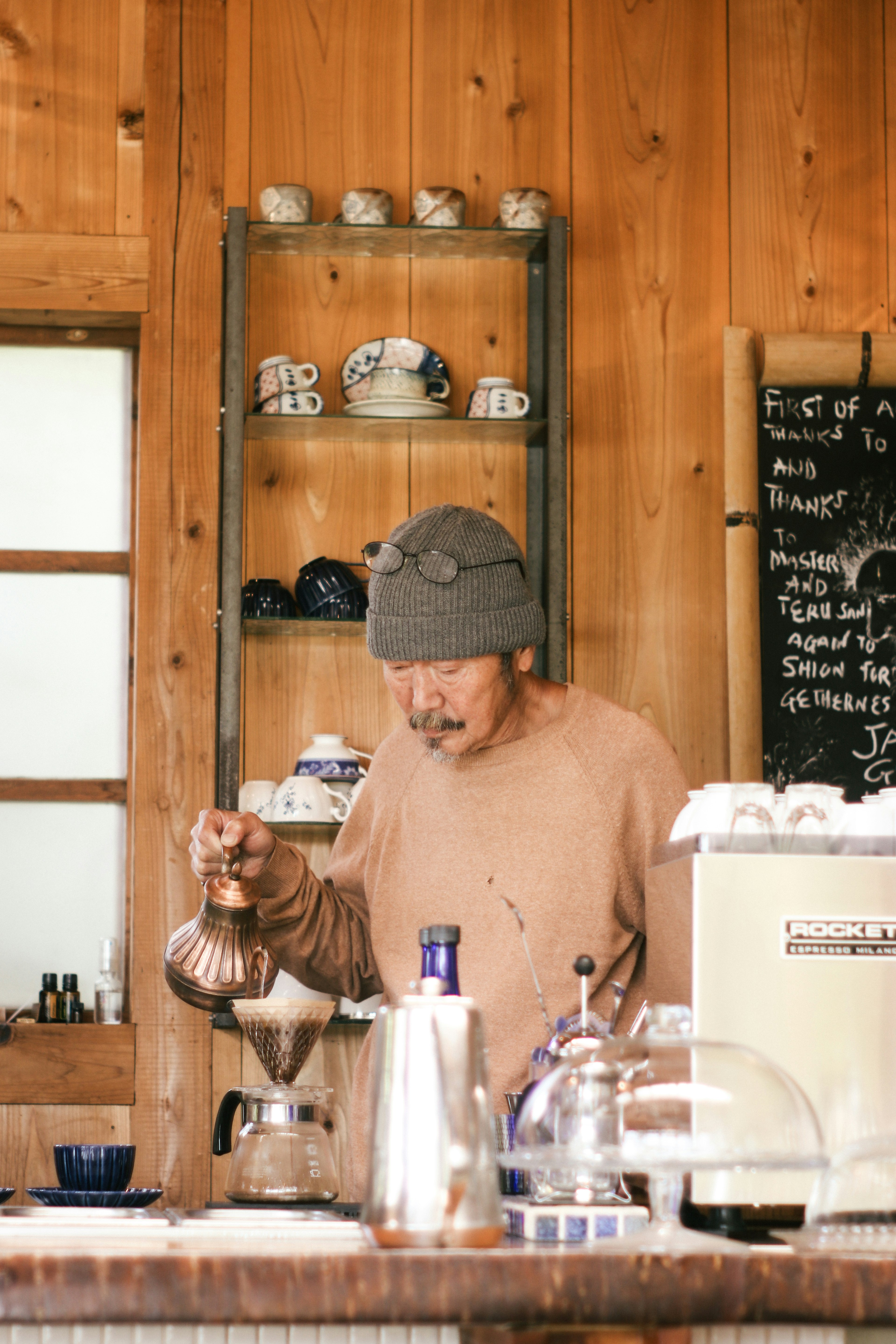 木製の壁に囲まれたカフェでコーヒーを淹れる男性