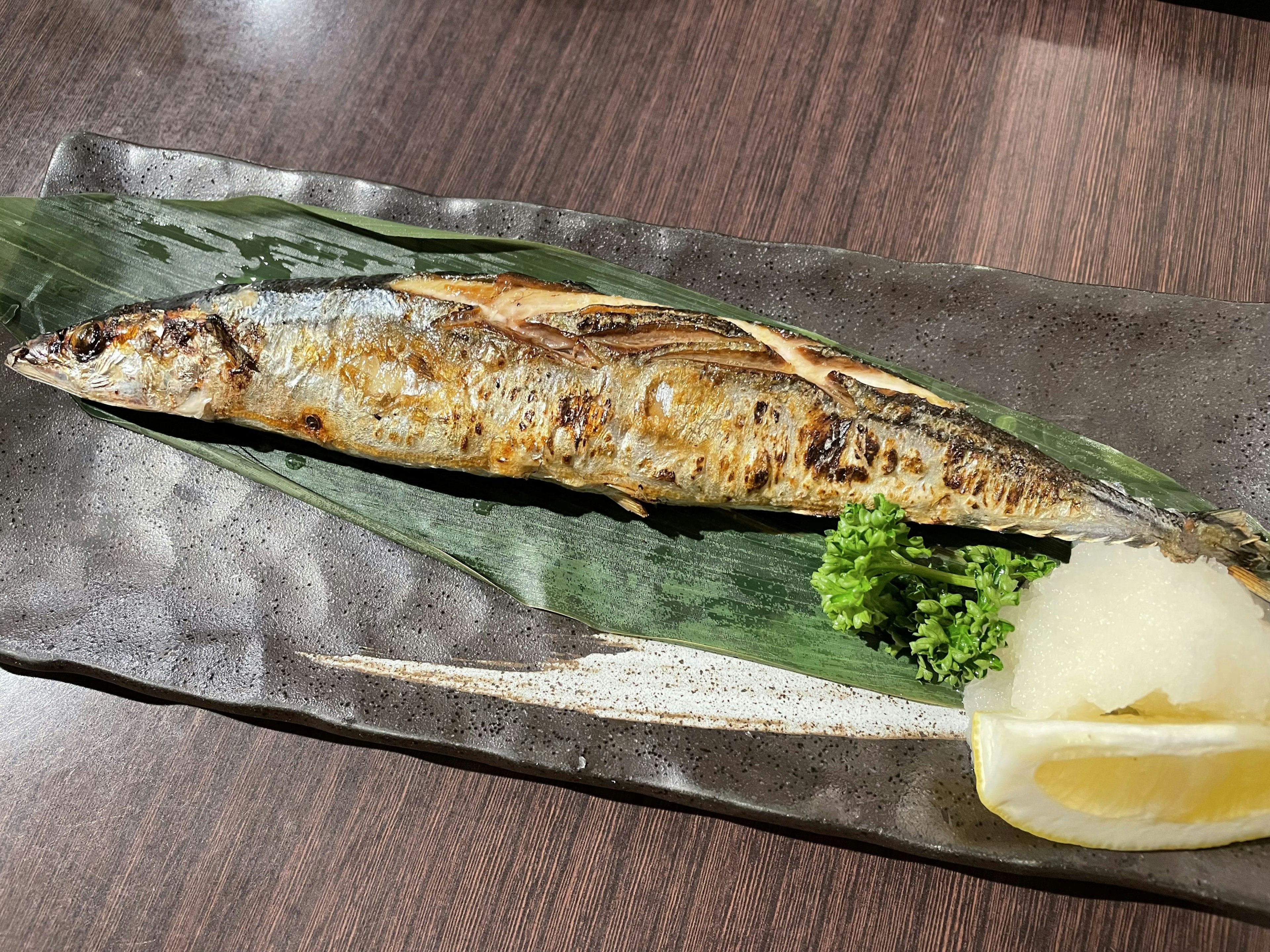 Presentasi ikan bakar dengan sanma dihias lemon dan daikon