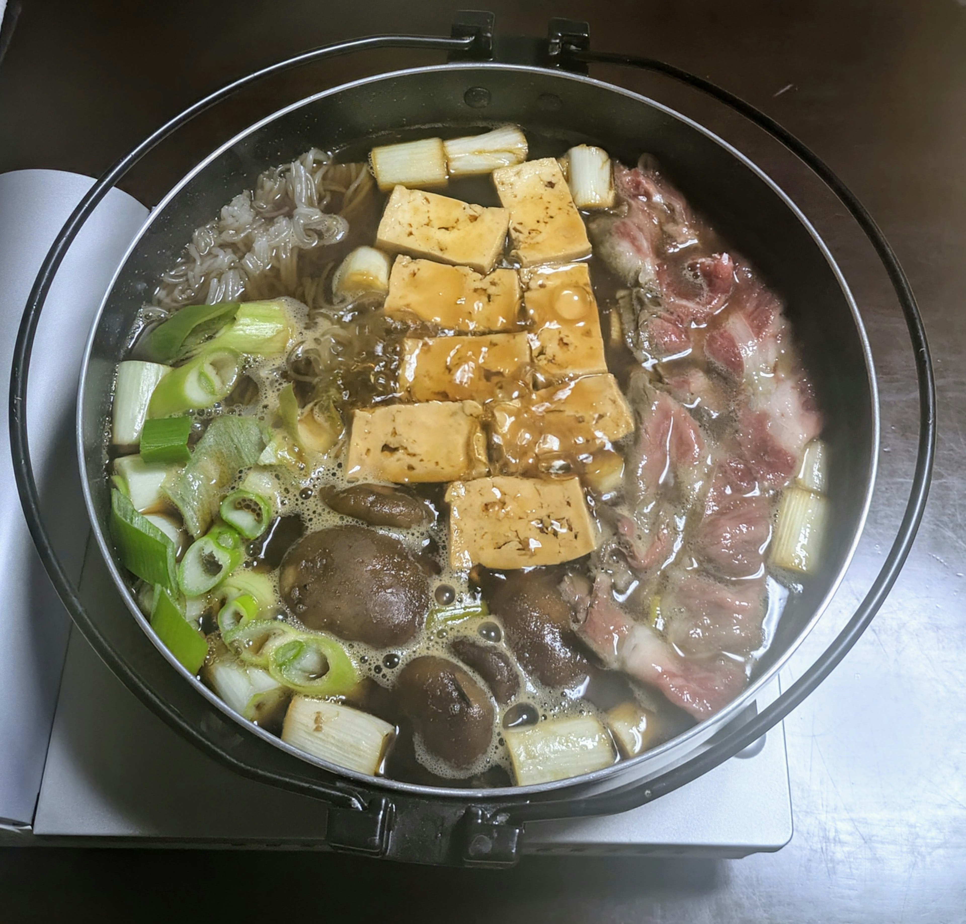 鍋料理の中に豆腐、ネギ、きのこ、肉が入った美味しそうな料理