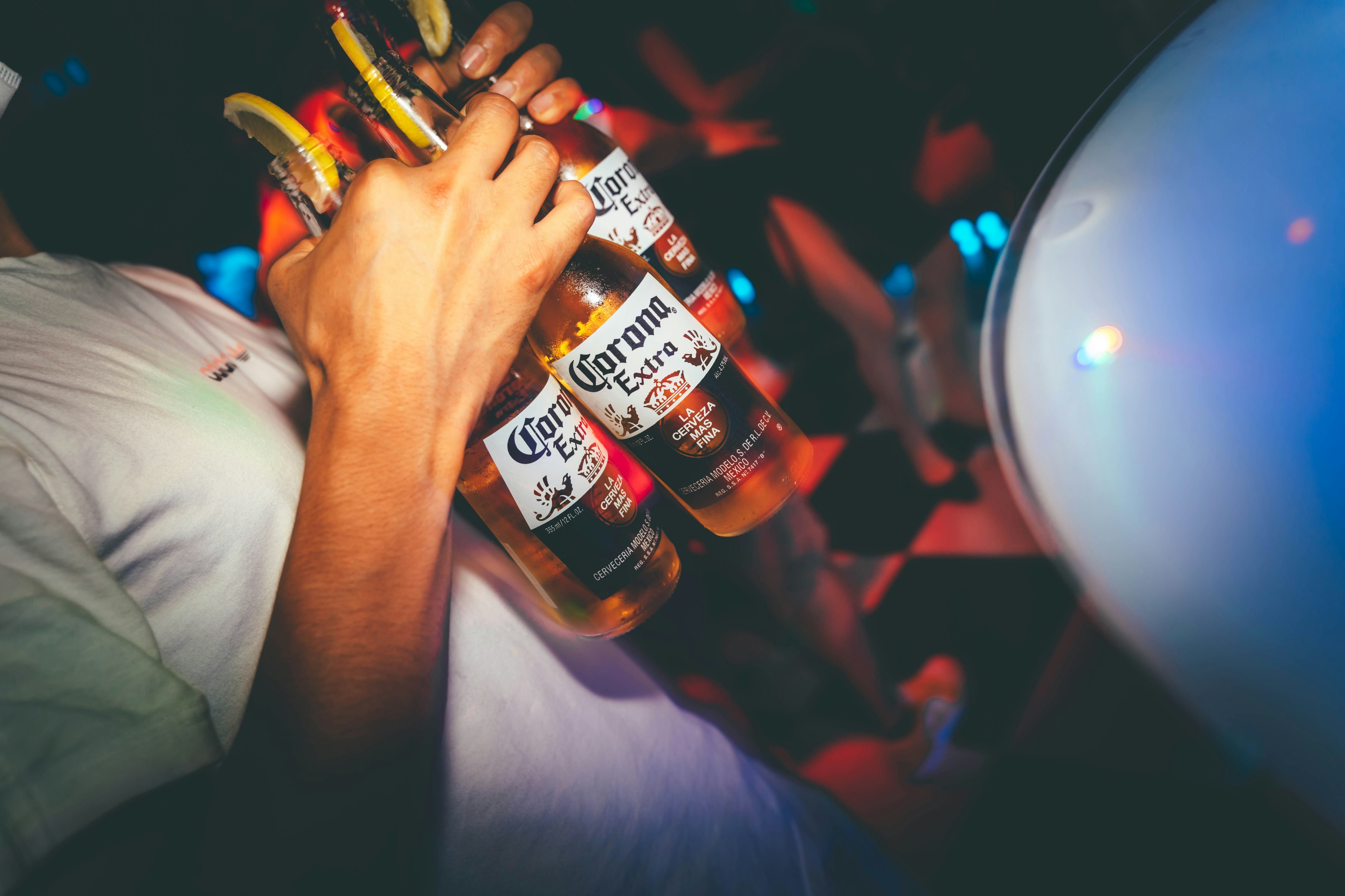 Person holding Corona beer bottles with a colorful party background