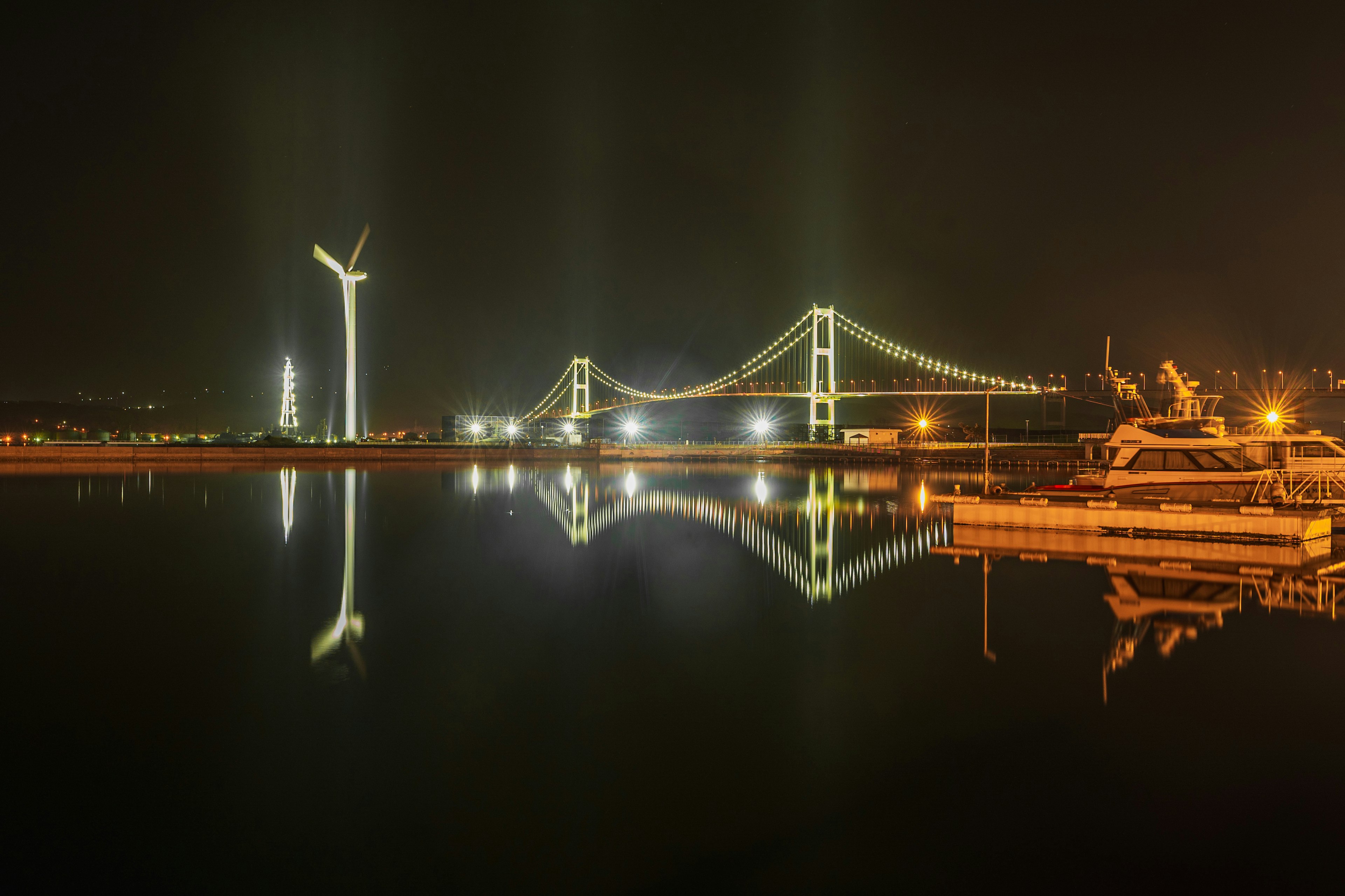 夜の水面に映る橋と風力発電機の風景