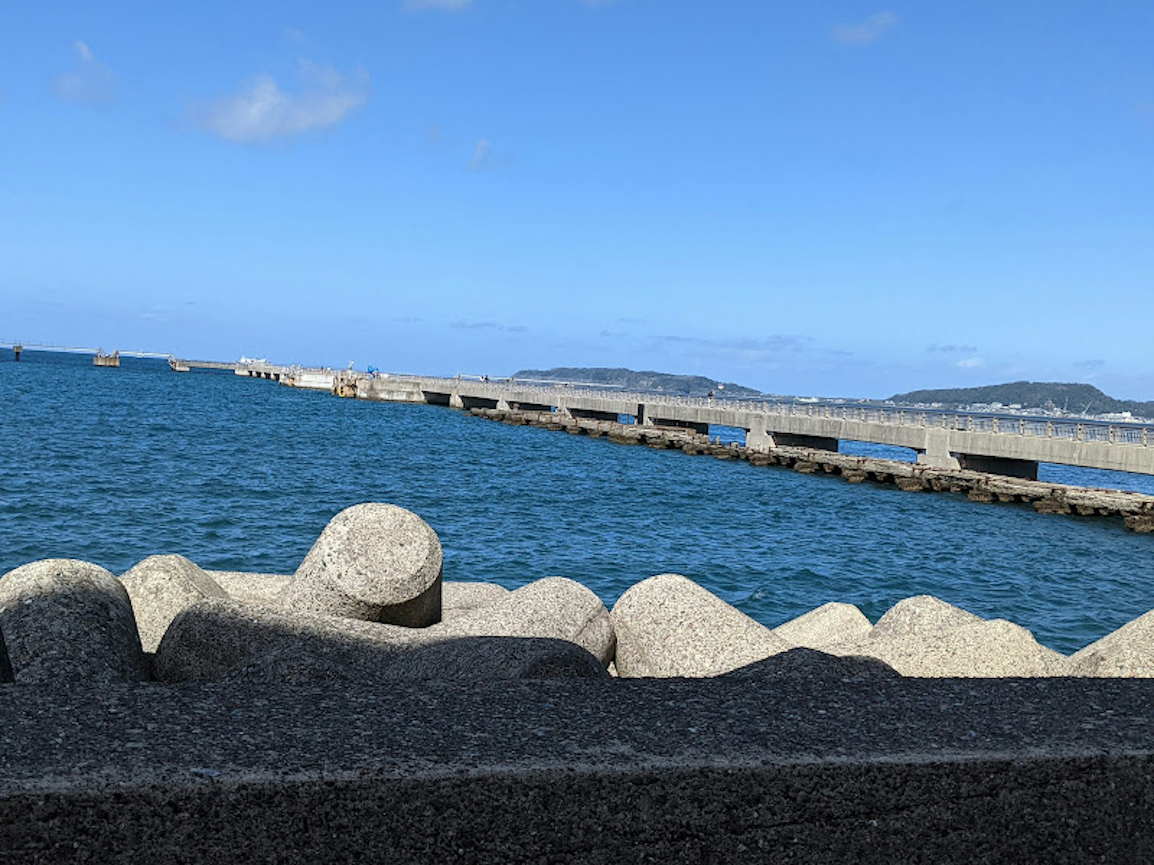 在晴朗天空下延伸至蓝色海洋的码头和岩石海岸